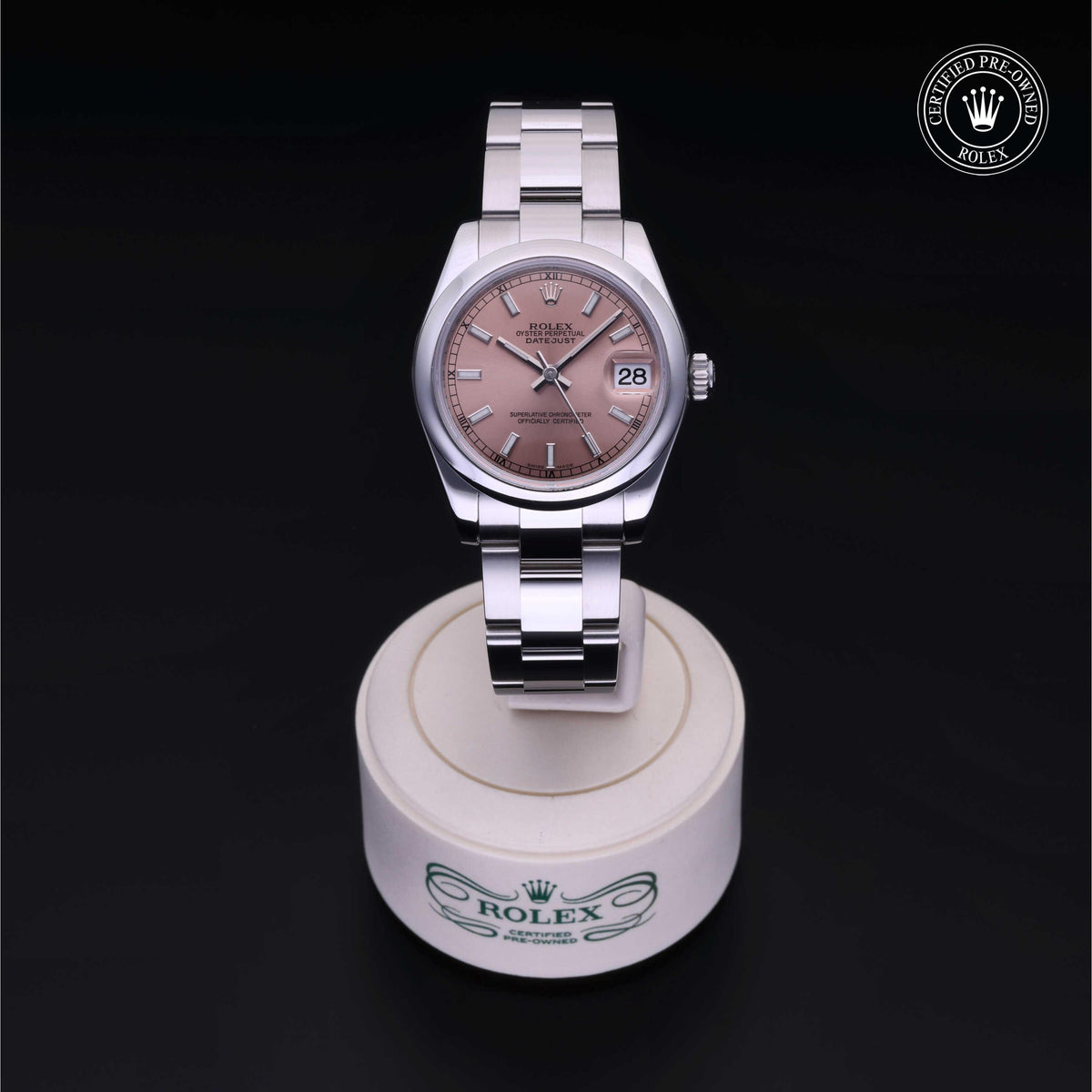 A Rolex certified pre-owned luxury watch with a stainless steel bracelet and a pink dial, displayed on a branded white stand against a black background.