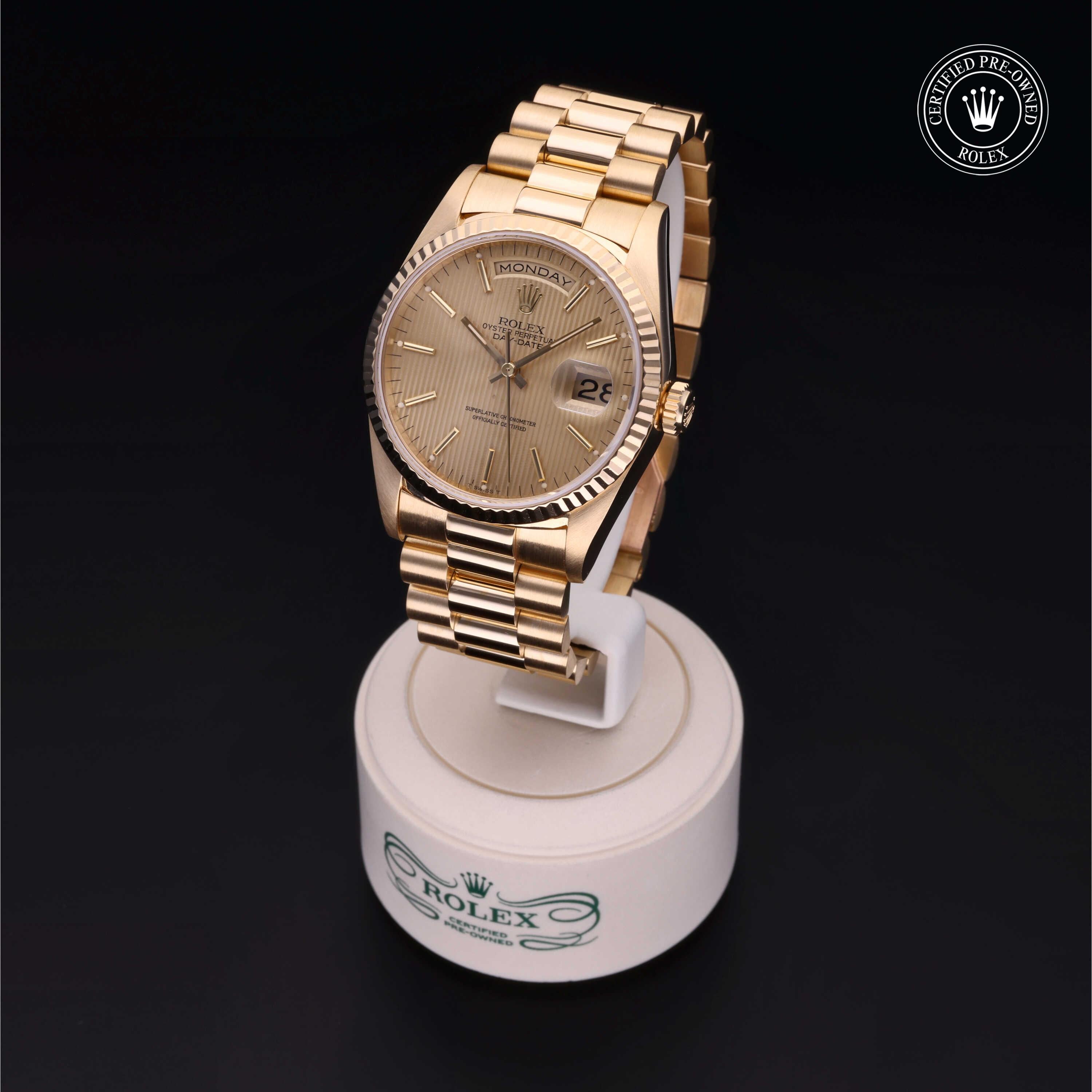 Gold-tone Rolex watch with a fluted bezel and day-date display, mounted on a white stand against a black background, showcasing luxury craftsmanship and Rolex certification.