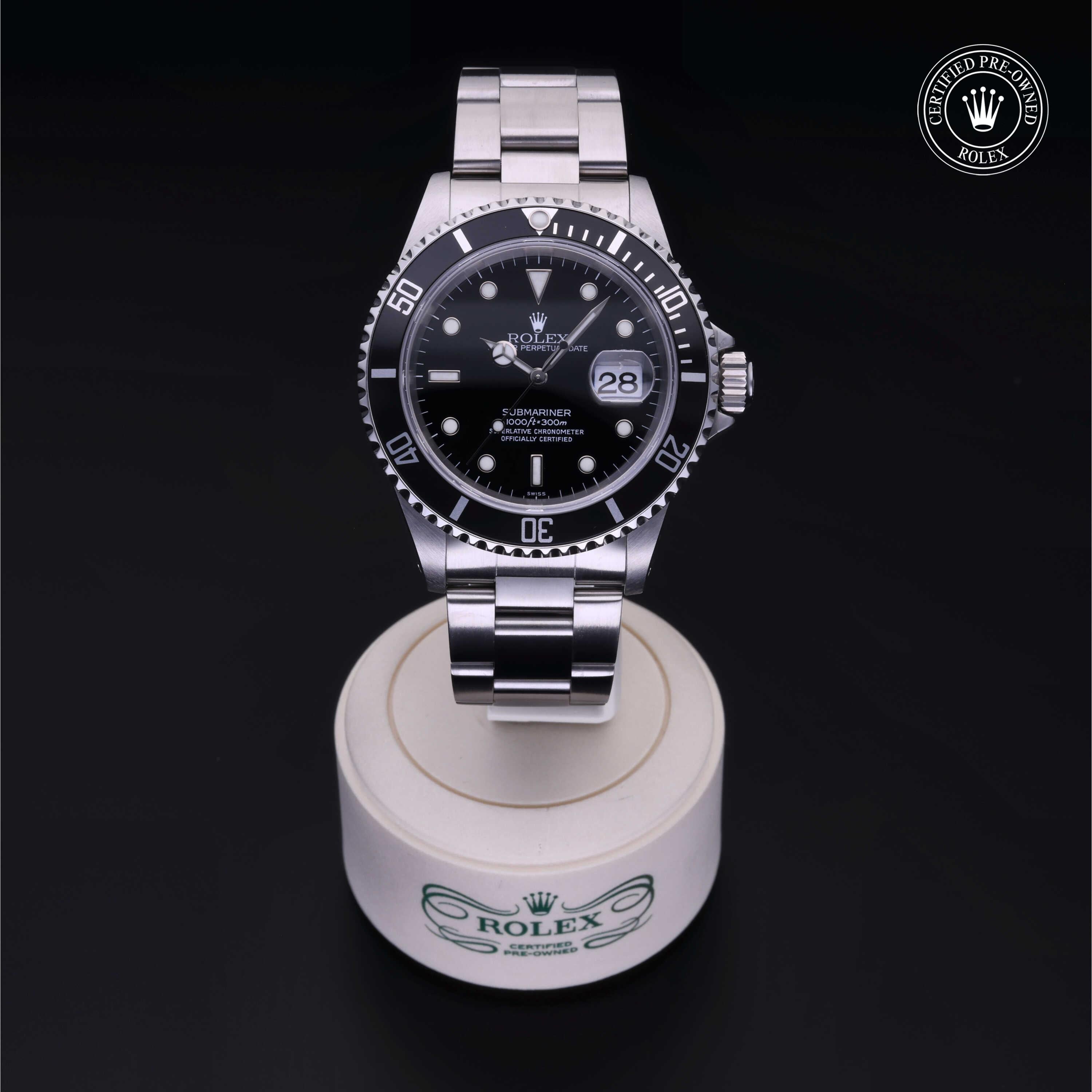 A luxury Rolex Submariner watch with a black dial and silver metal bracelet displayed on a white stand with the Rolex logo, featuring a certified pre-owned badge.