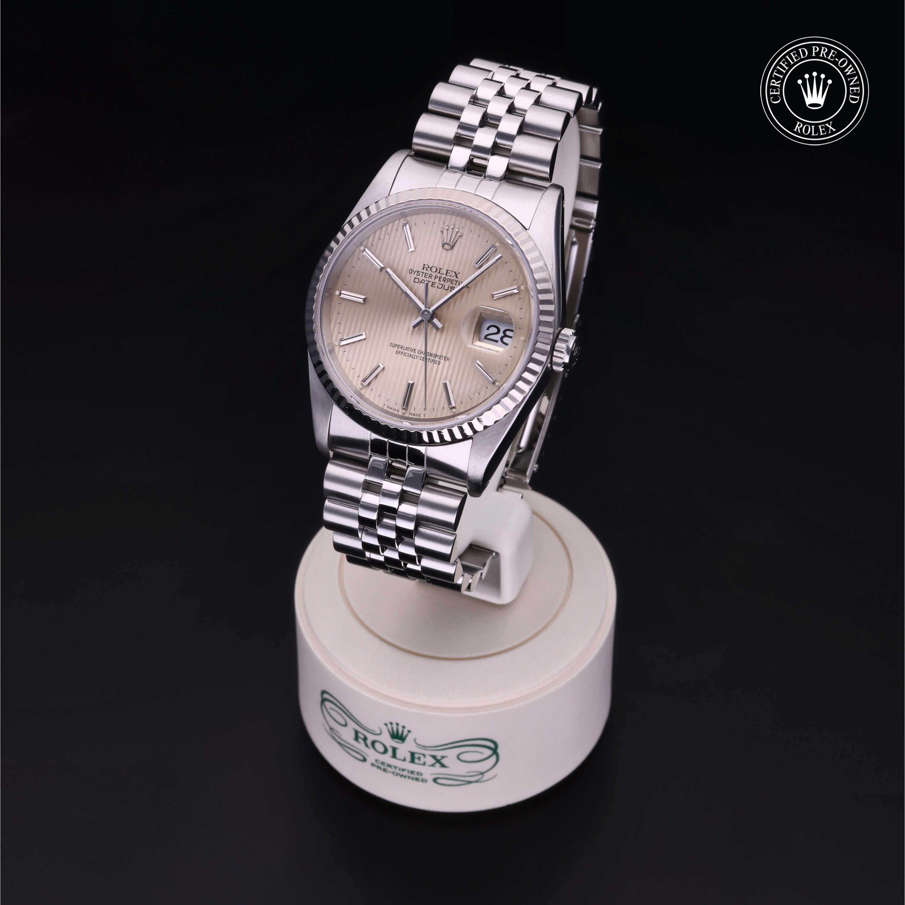 Rolex luxury watch with silver fluted bezel and jubilee bracelet displayed on a white stand with Rolex logo, showcasing precision and timeless design from a certified pre-owned collection.