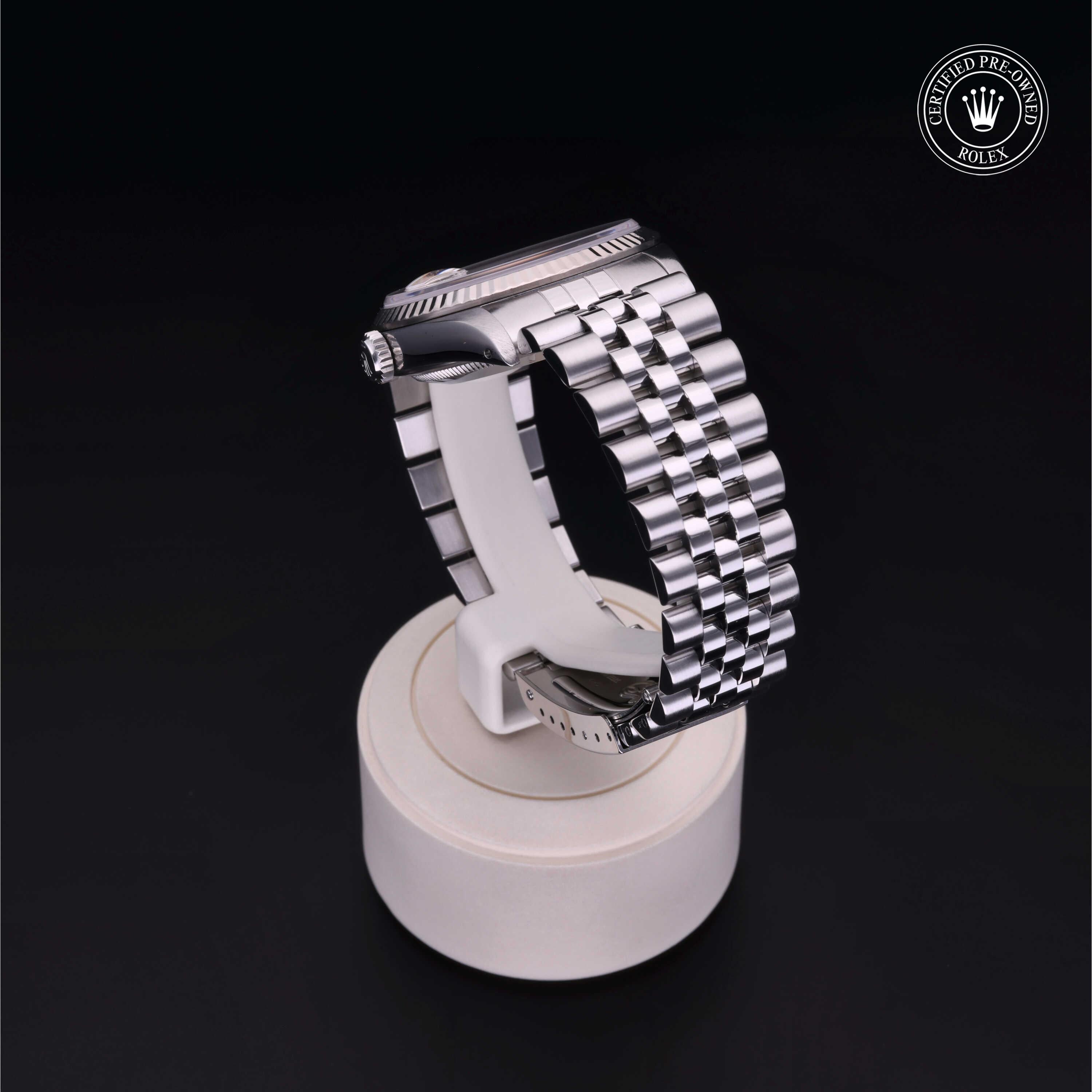 Close-up of a silver metal bracelet with a polished finish displayed on a white cylindrical stand against a black background, featuring a Rolex Certified Pre-Owned logo in the corner.