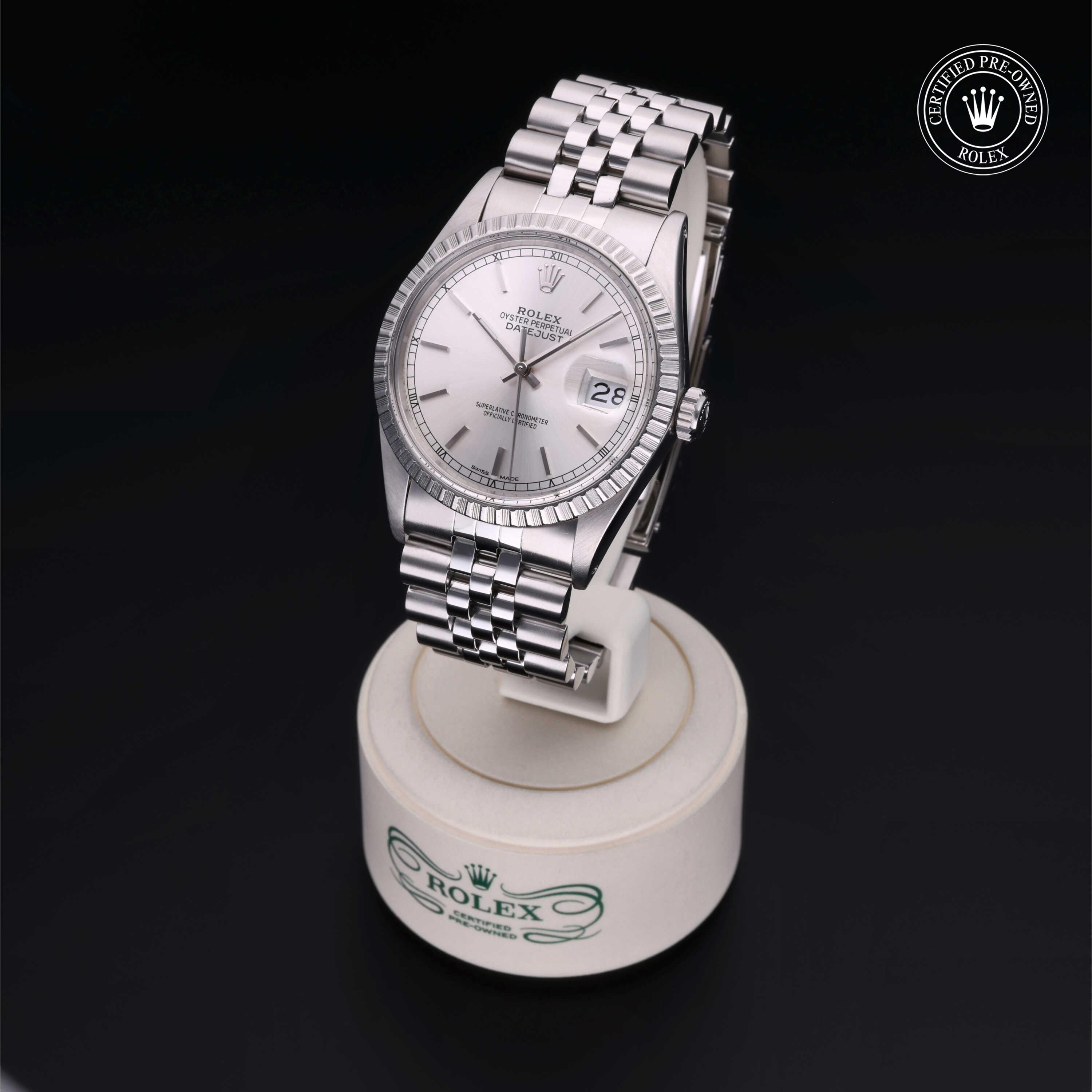 Silver Rolex wristwatch with a fluted bezel and date display on a Jubilee bracelet, displayed on a branded stand with a certified pre-owned Rolex logo in the corner.