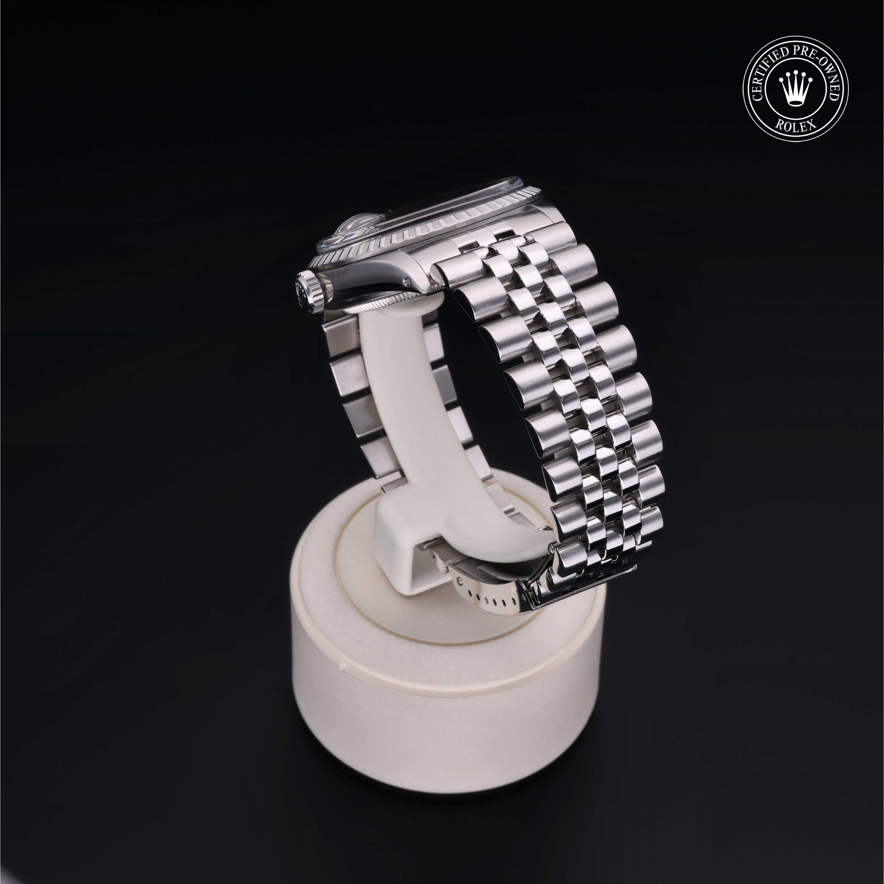 Silver-tone Rolex watch with a polished Jubilee bracelet displayed on a white stand against a black background, featuring a certified pre-owned Rolex logo.