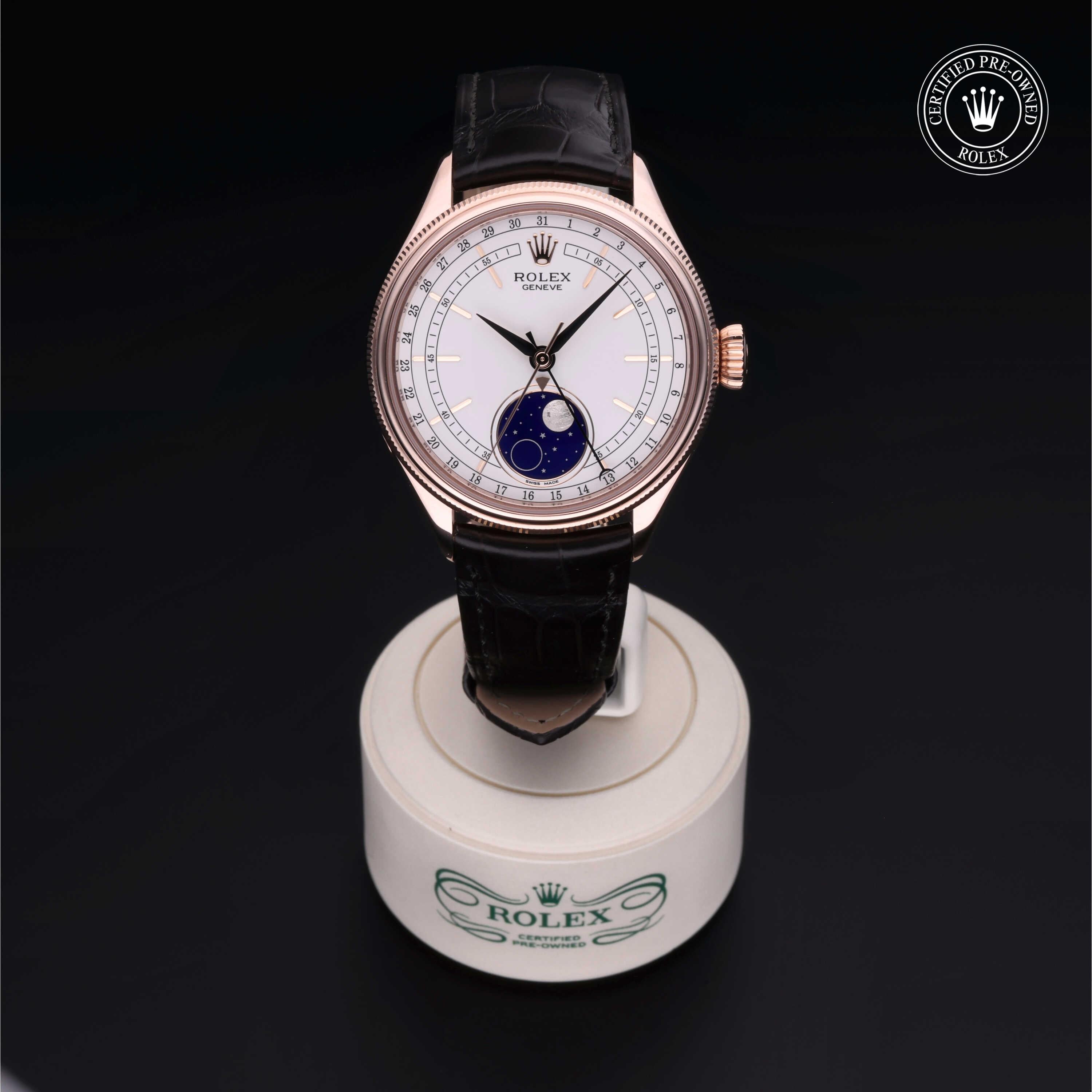 Rolex watch with a white dial, gold case, black leather strap, and moonphase complication, displayed on a branded stand with a certified pre-owned logo.