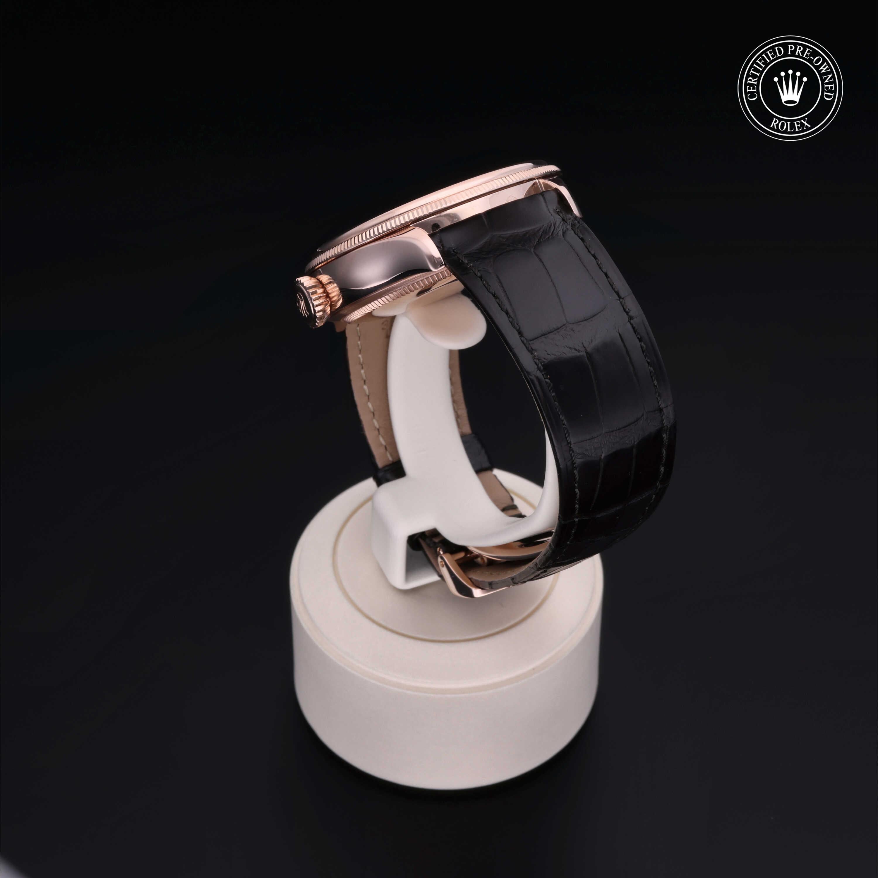 Side view of a luxury wristwatch with a rose gold case and black alligator leather strap displayed on a white stand against a black background, featuring a certified pre-owned Rolex badge.