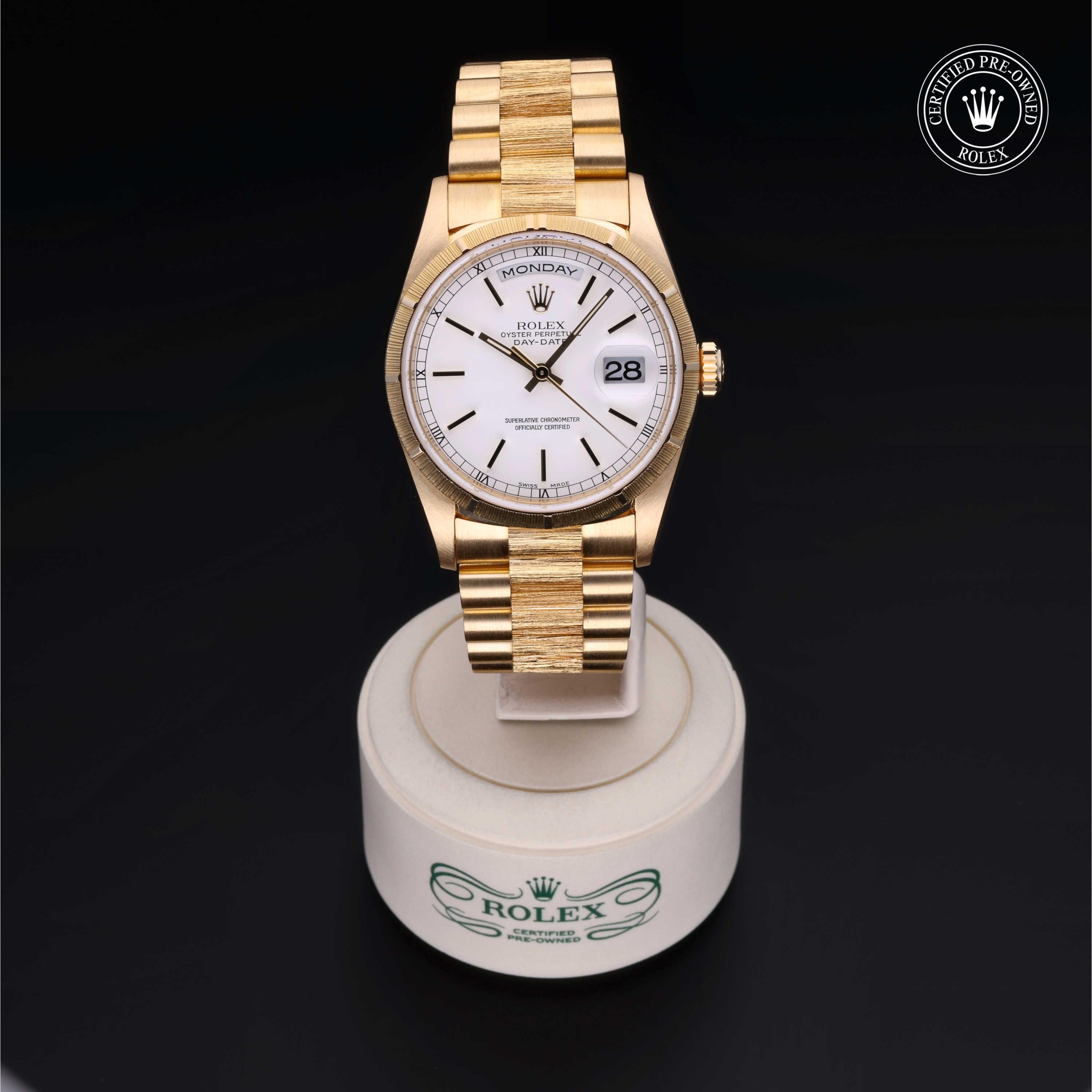 Elegant gold Rolex watch with a white dial showing day and date, displayed on a branded stand with a certified pre-owned Rolex logo in the corner.