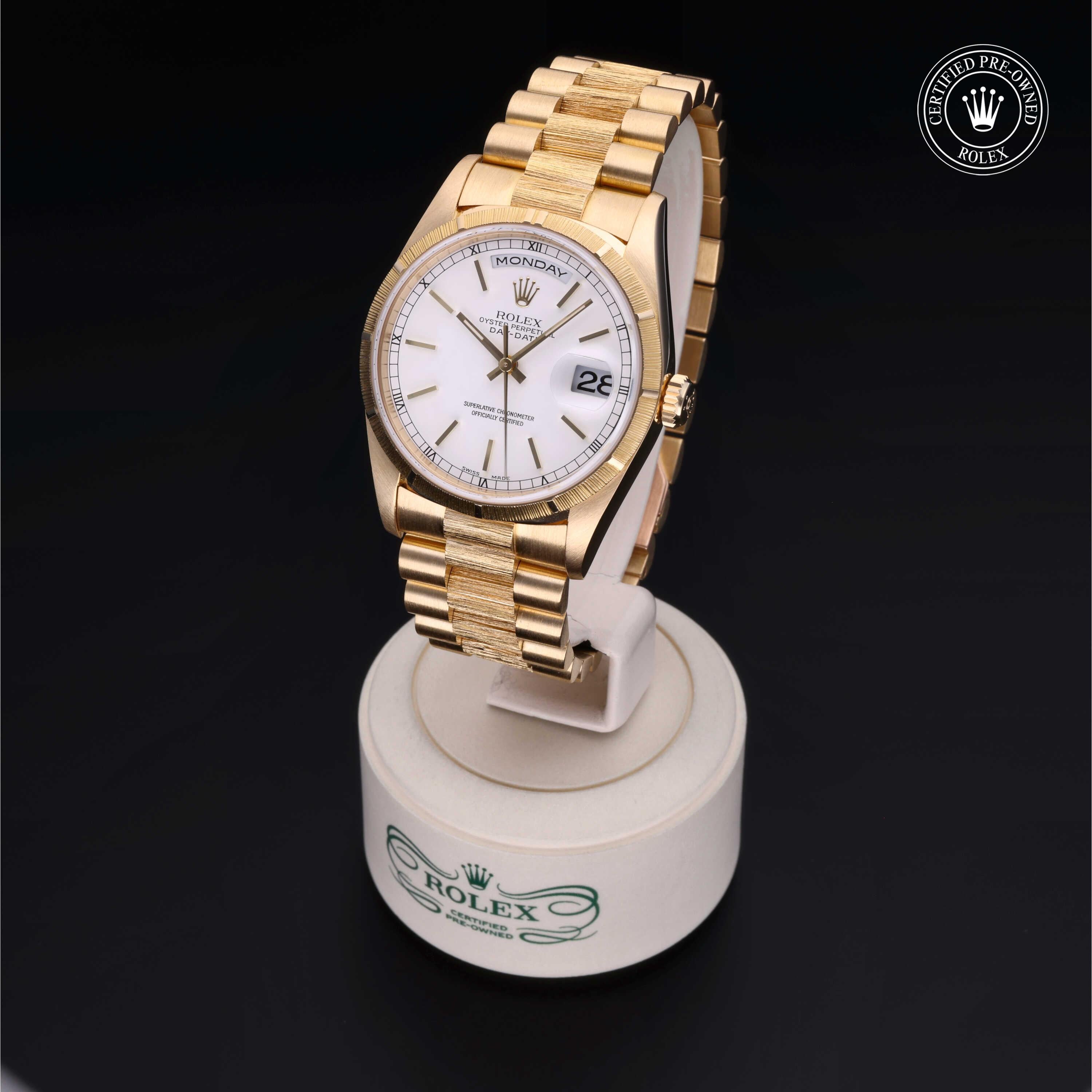 Close-up of a luxury gold Rolex watch with a white dial and day-date display on a white stand with Rolex branding, showcasing fine craftsmanship and elegance.