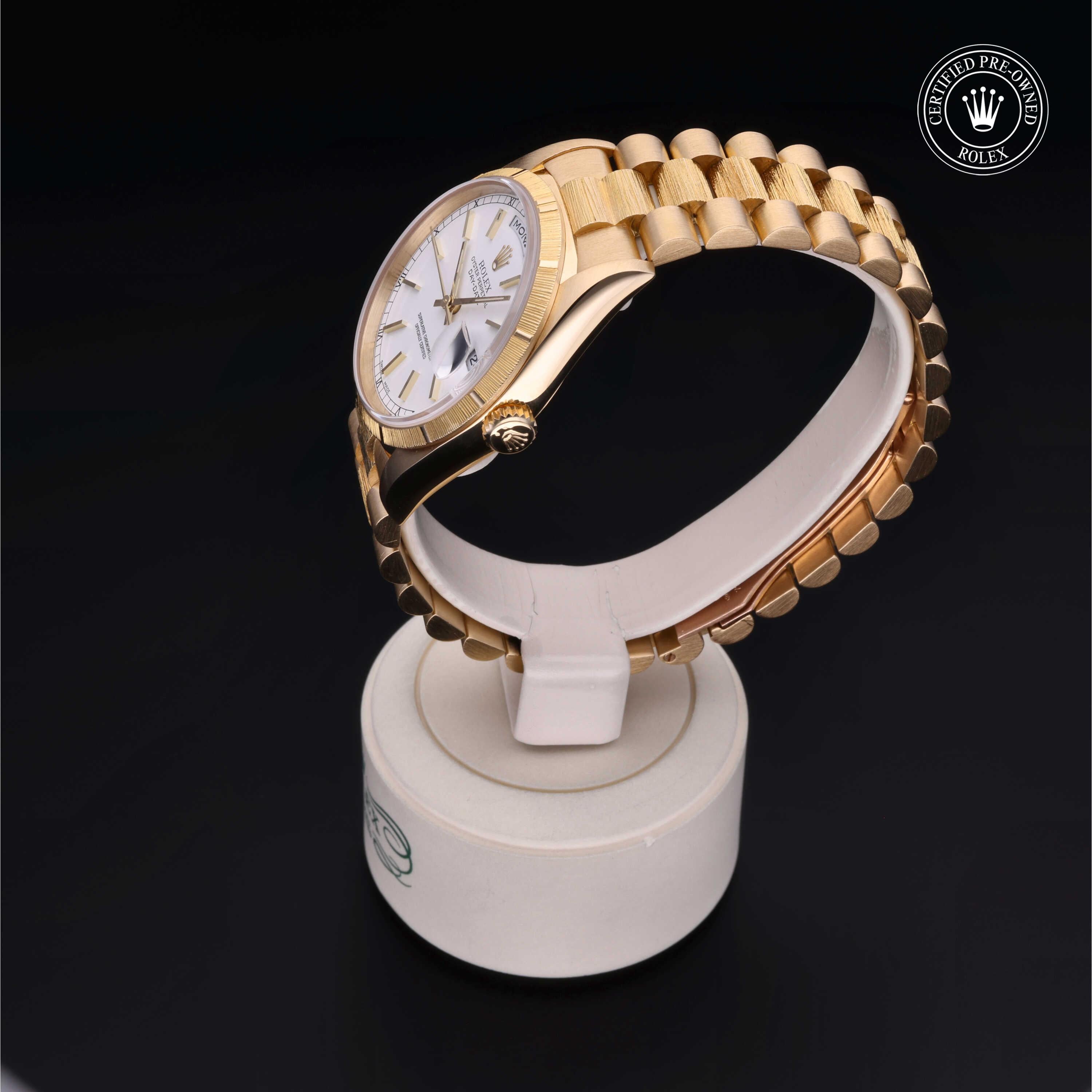 Close-up of a gold Rolex wristwatch with a white dial and date display, showcased on a white stand against a black background with a certified pre-owned Rolex logo.