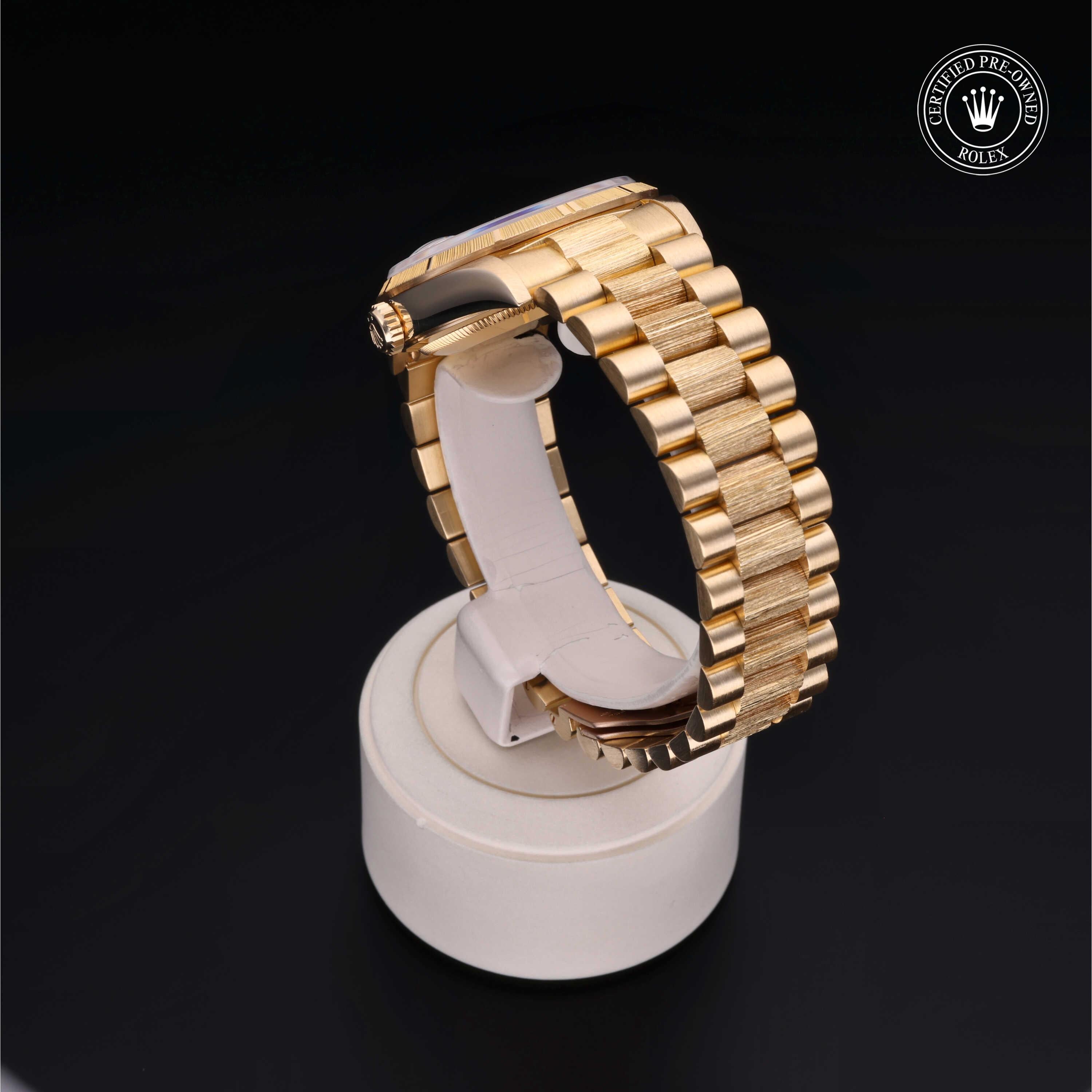 Gold-tone luxury watch band displayed on a white stand against a black background, featuring a certified pre-owned Rolex logo in the corner.