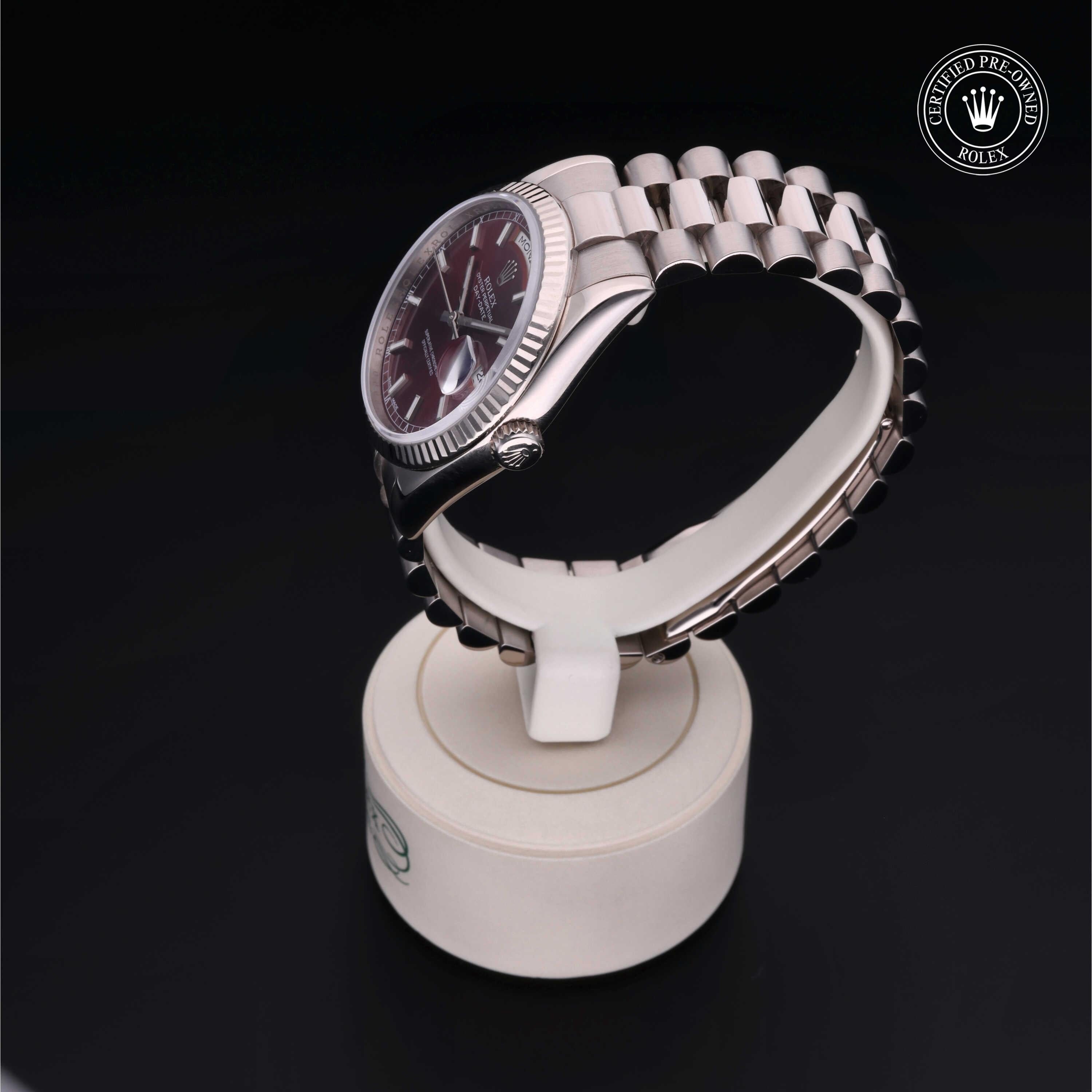 Silver Rolex luxury watch with a burgundy dial and jubilee bracelet displayed on a white stand, featured with a certified pre-owned Rolex logo on a black background.