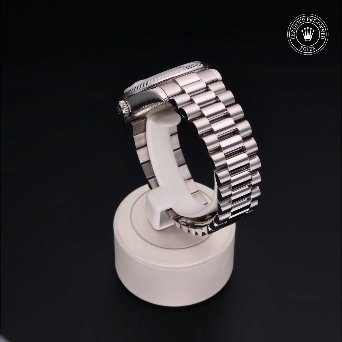 A polished stainless steel Rolex watch with a linked bracelet displayed on a white stand against a black background, featuring a Certified Pre-Owned Rolex logo in the corner.