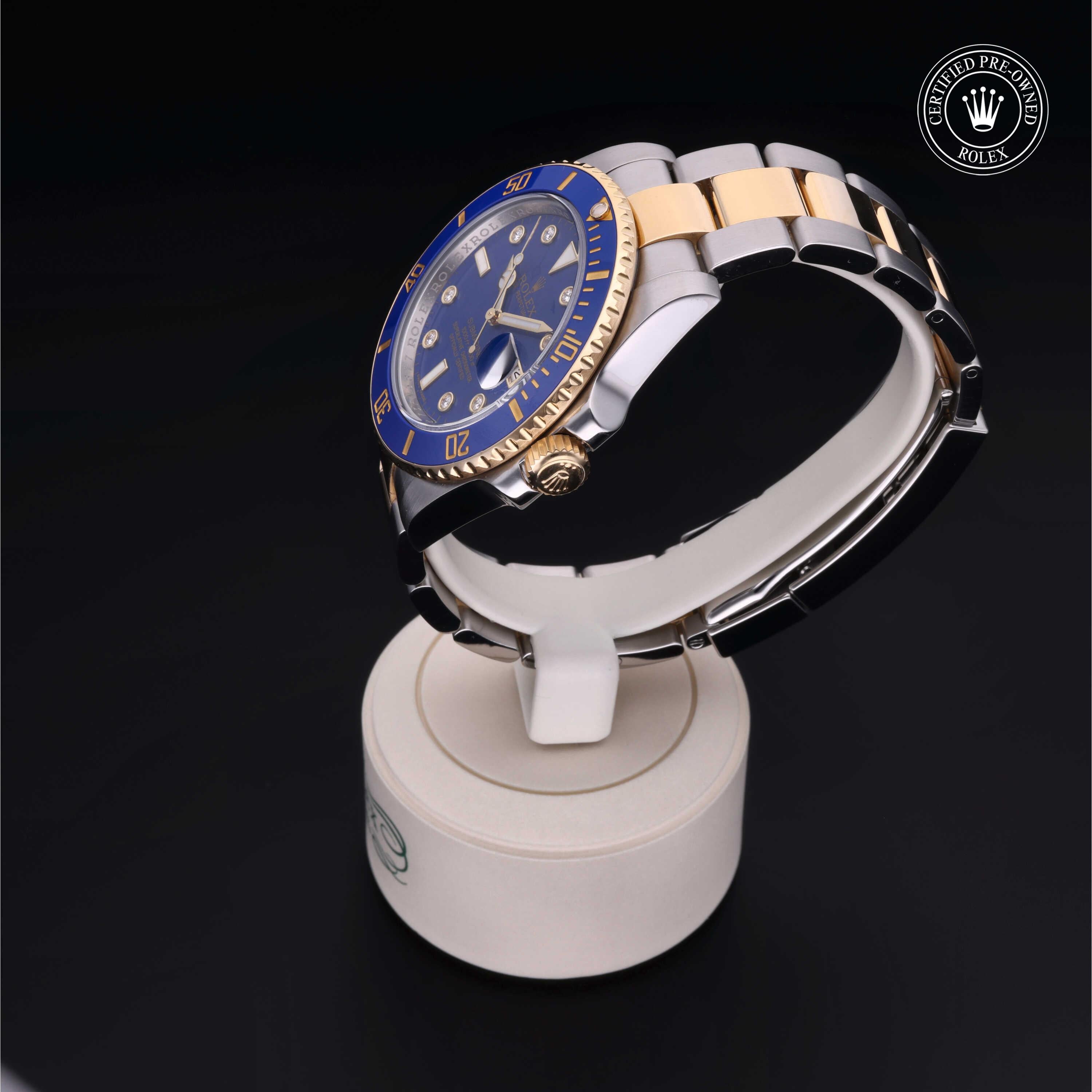 Close-up of a luxury two-tone Rolex watch with a blue dial and gold accents displayed on a white stand against a black background, featuring a certified pre-owned Rolex seal.