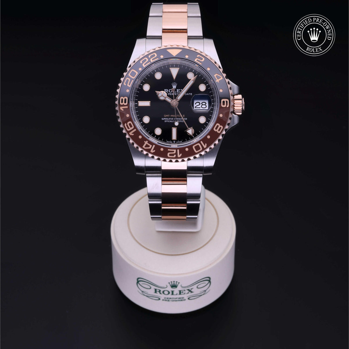 Rolex GMT-Master II watch with two-tone stainless steel and rose gold bracelet, black dial, date display, and rotating bezel, showcased on a branded stand.