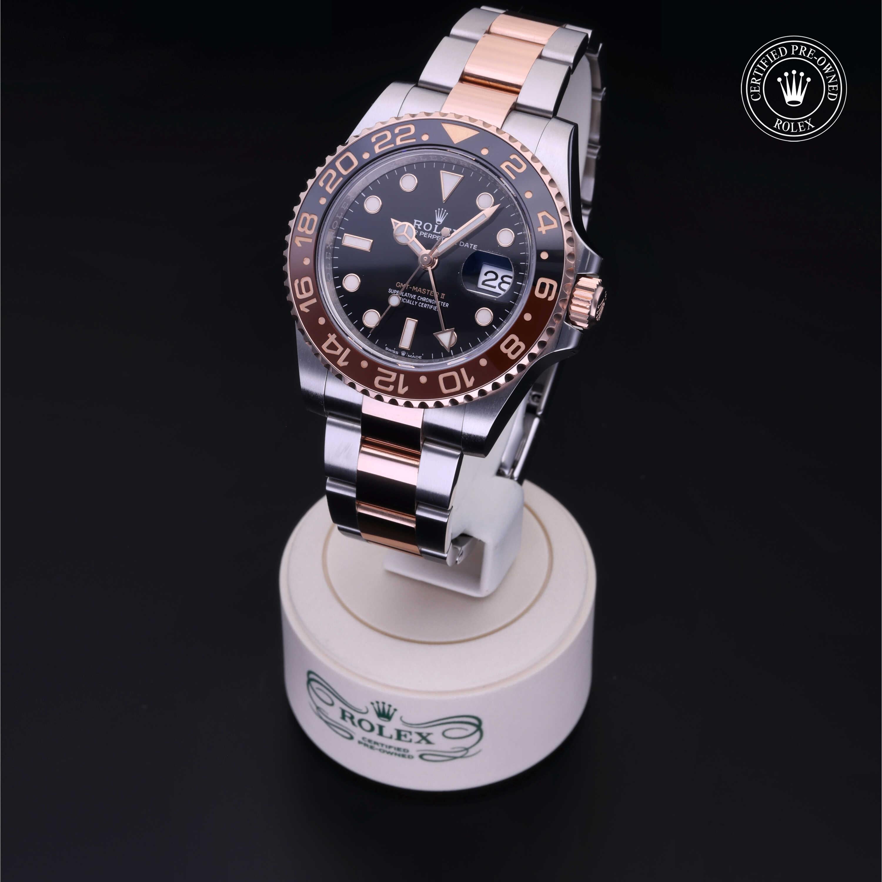 Two-tone Rolex luxury watch with a black dial and rose gold accents displayed on a branded stand, featuring a date window and GMT function, emphasizing fine jewelry and craftsmanship.