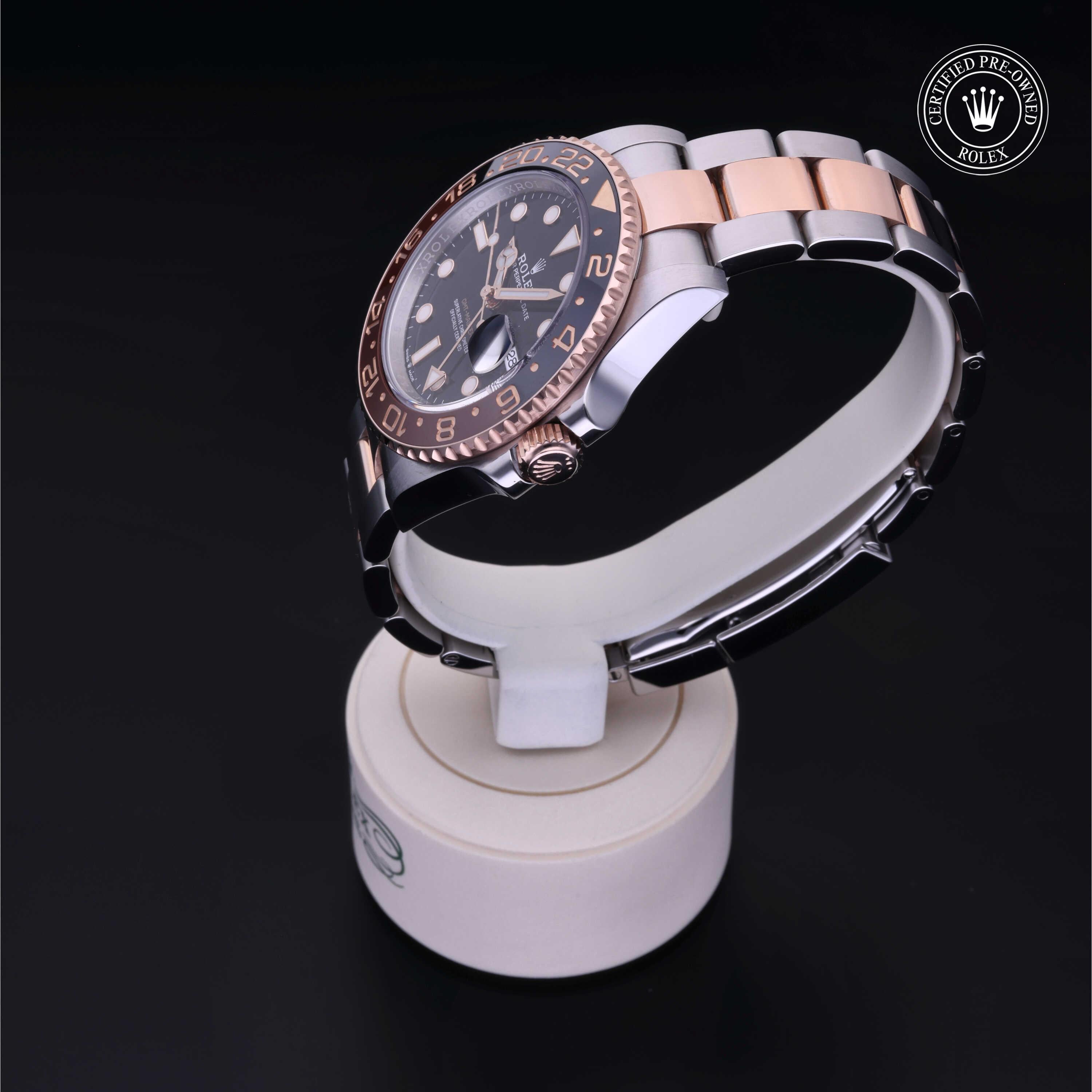 Rolex luxury watch with a two-tone metal band displayed on a white stand, featuring a black dial and bezel with rose gold accents, certified pre-owned emblem visible.