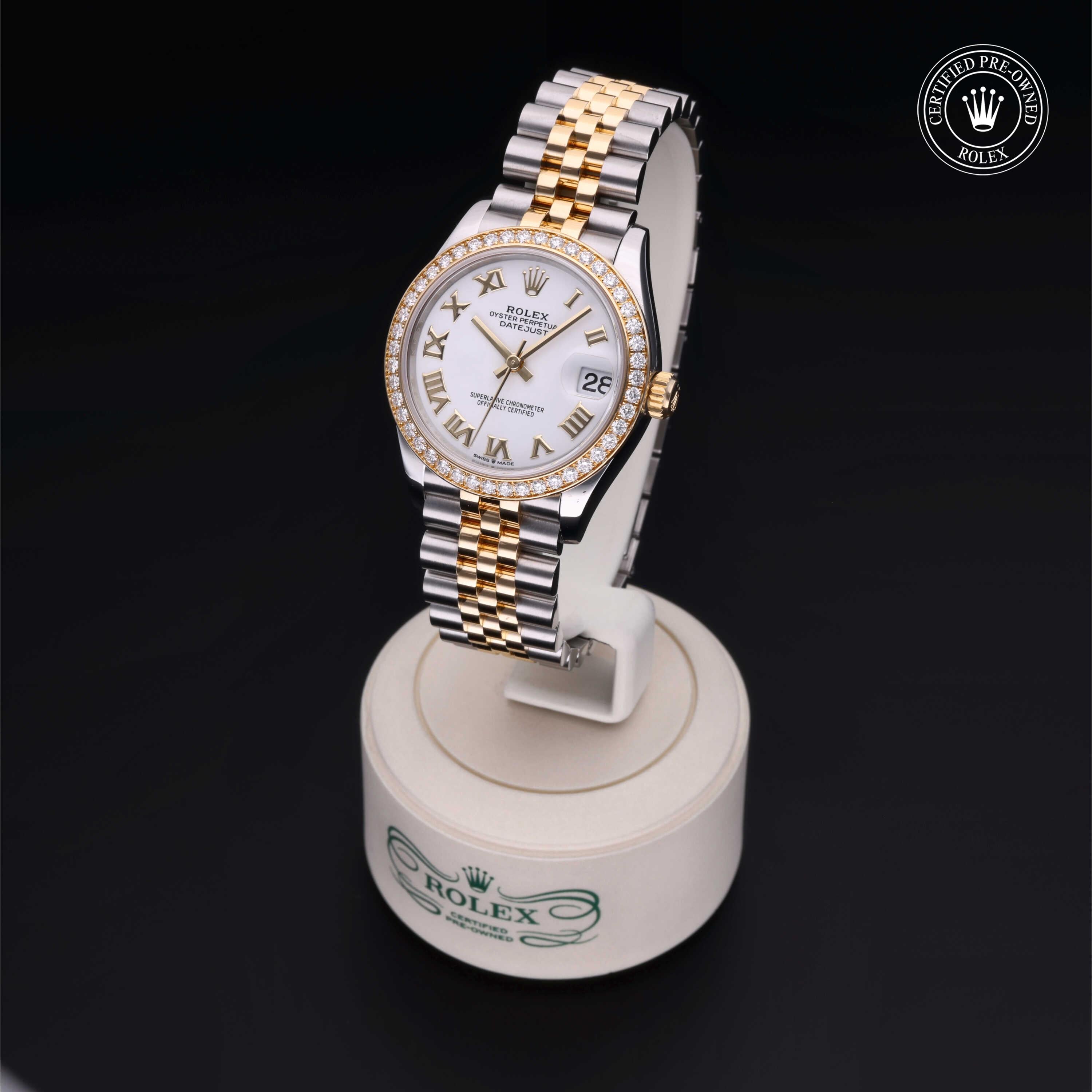 Two-tone Rolex watch with gold and silver bracelet, white dial with Roman numerals and diamond bezel, displayed on a branded stand with Certified Pre-Owned Rolex emblem.