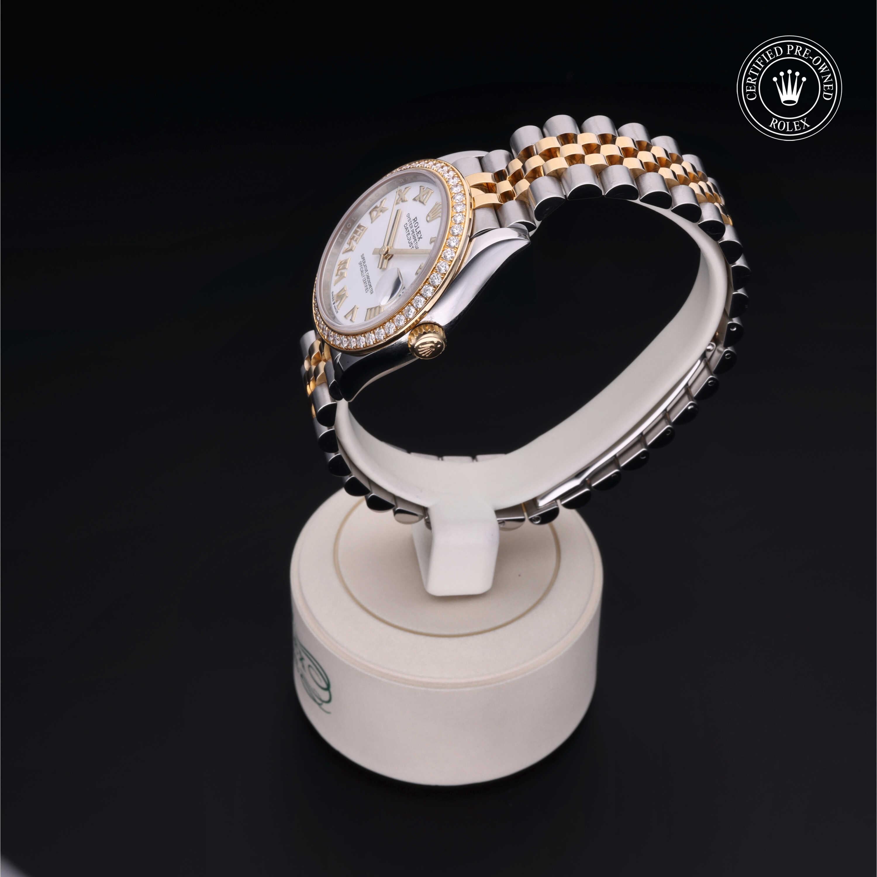 Two-tone Rolex wristwatch with a diamond bezel and patterned bracelet, displayed on a white stand against a black background, featuring a certified pre-owned Rolex logo.