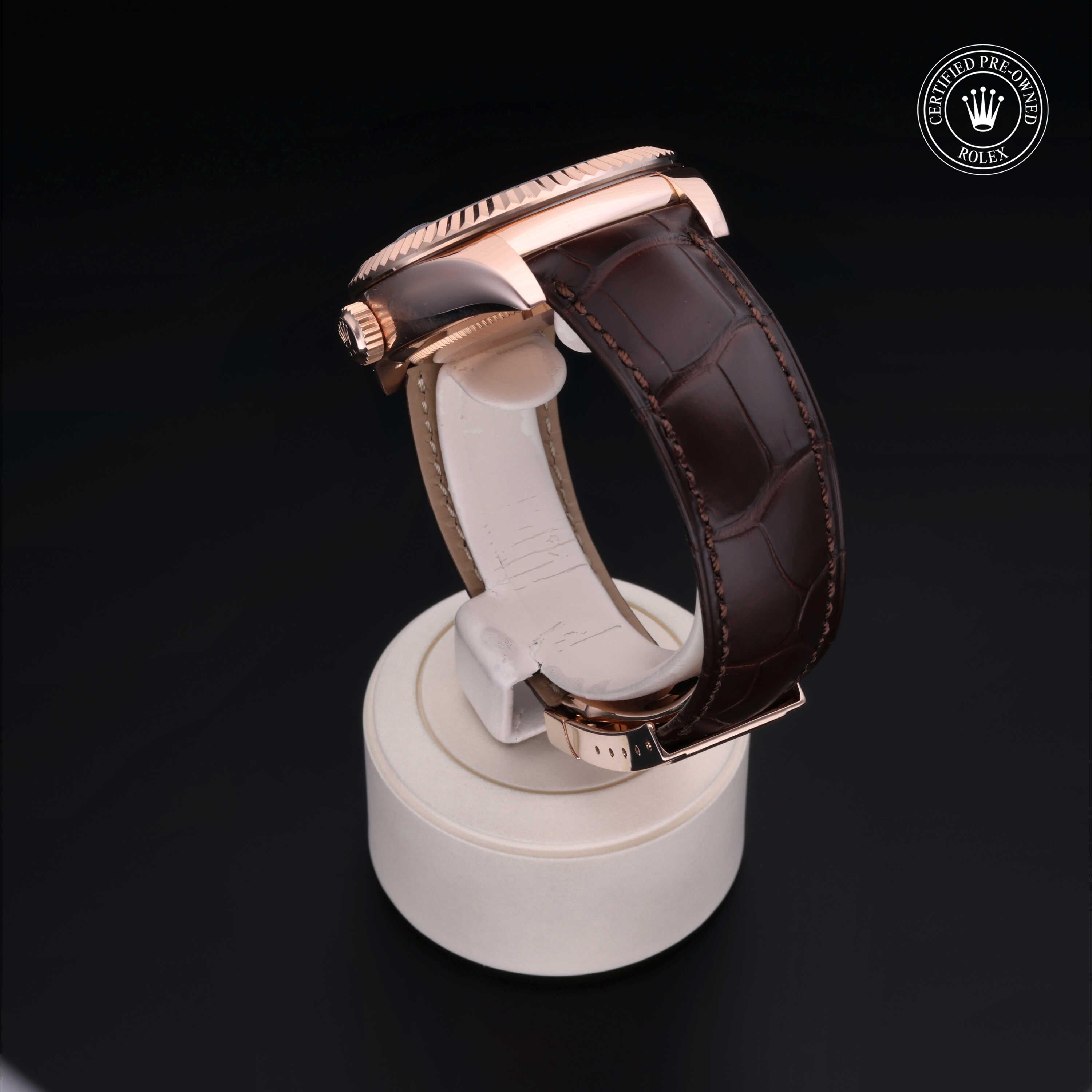 Rose gold luxury watch with a dark brown leather strap displayed on a white stand, featuring a certified pre-owned Rolex logo, highlighting fine craftsmanship and style.