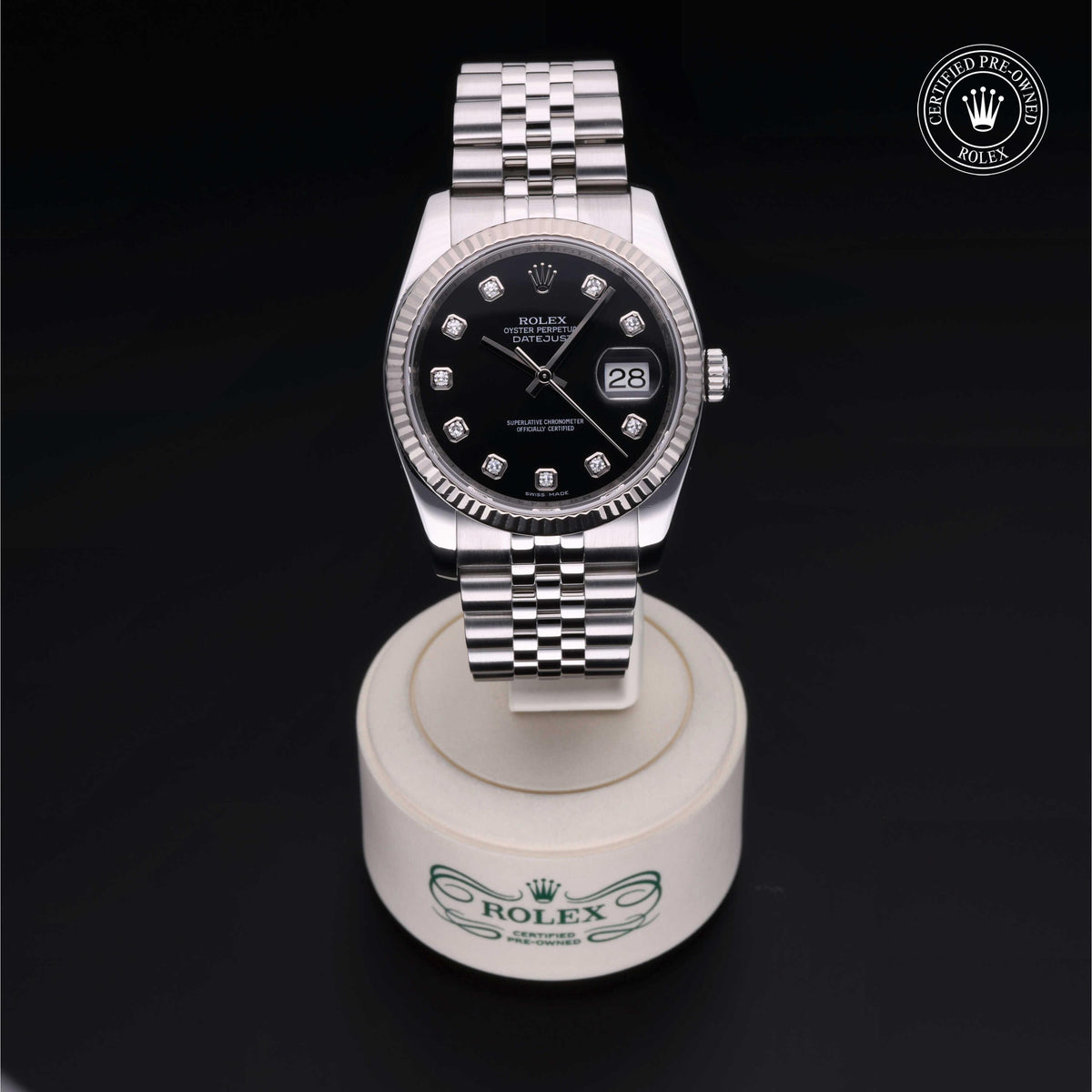 Rolex stainless steel luxury watch with black dial and diamond hour markers displayed on a branded stand, featuring a certified pre-owned Rolex logo.