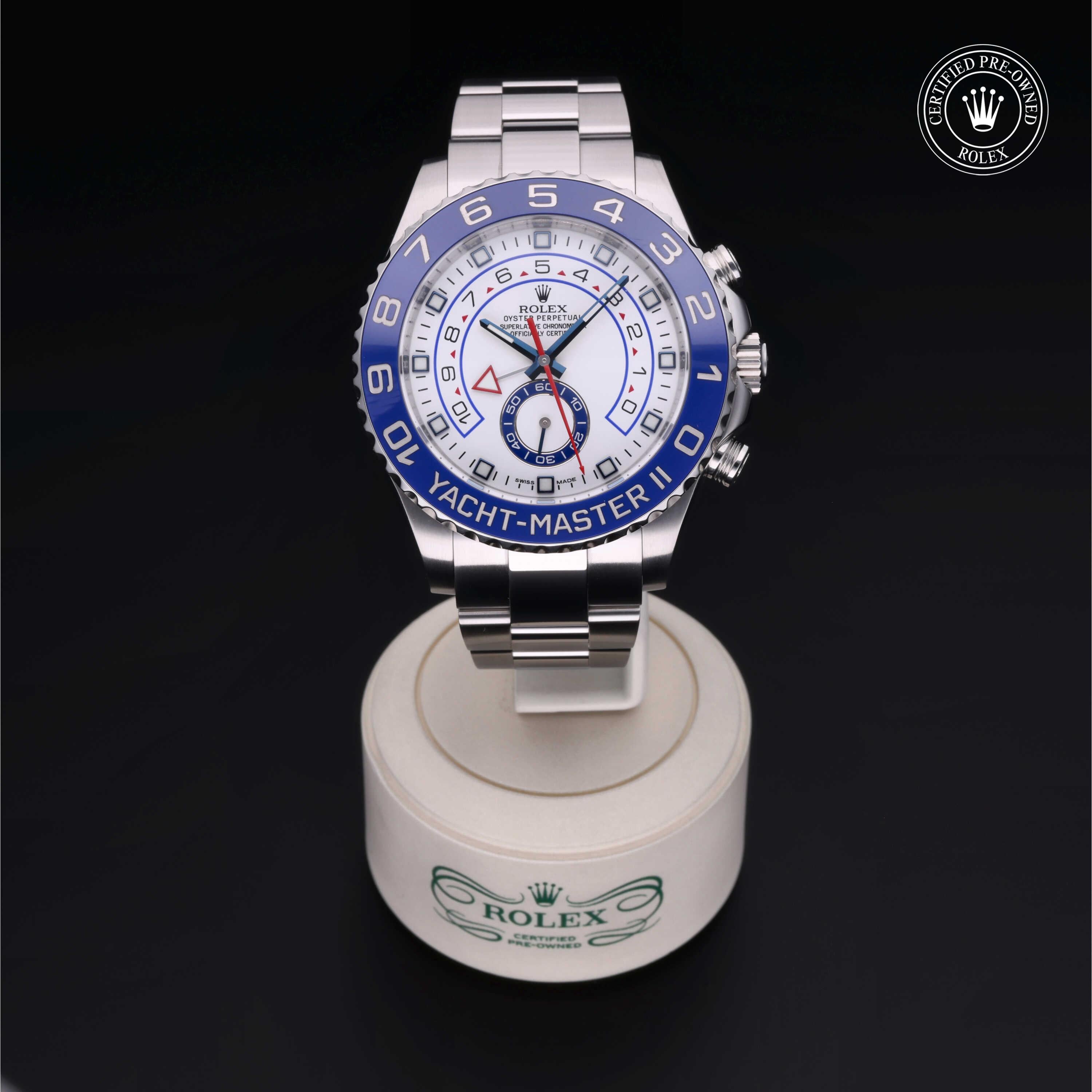 A luxury Rolex Yacht-Master II watch with a blue and white dial displayed on a branded stand, featuring chronograph functions and a stainless steel bracelet.