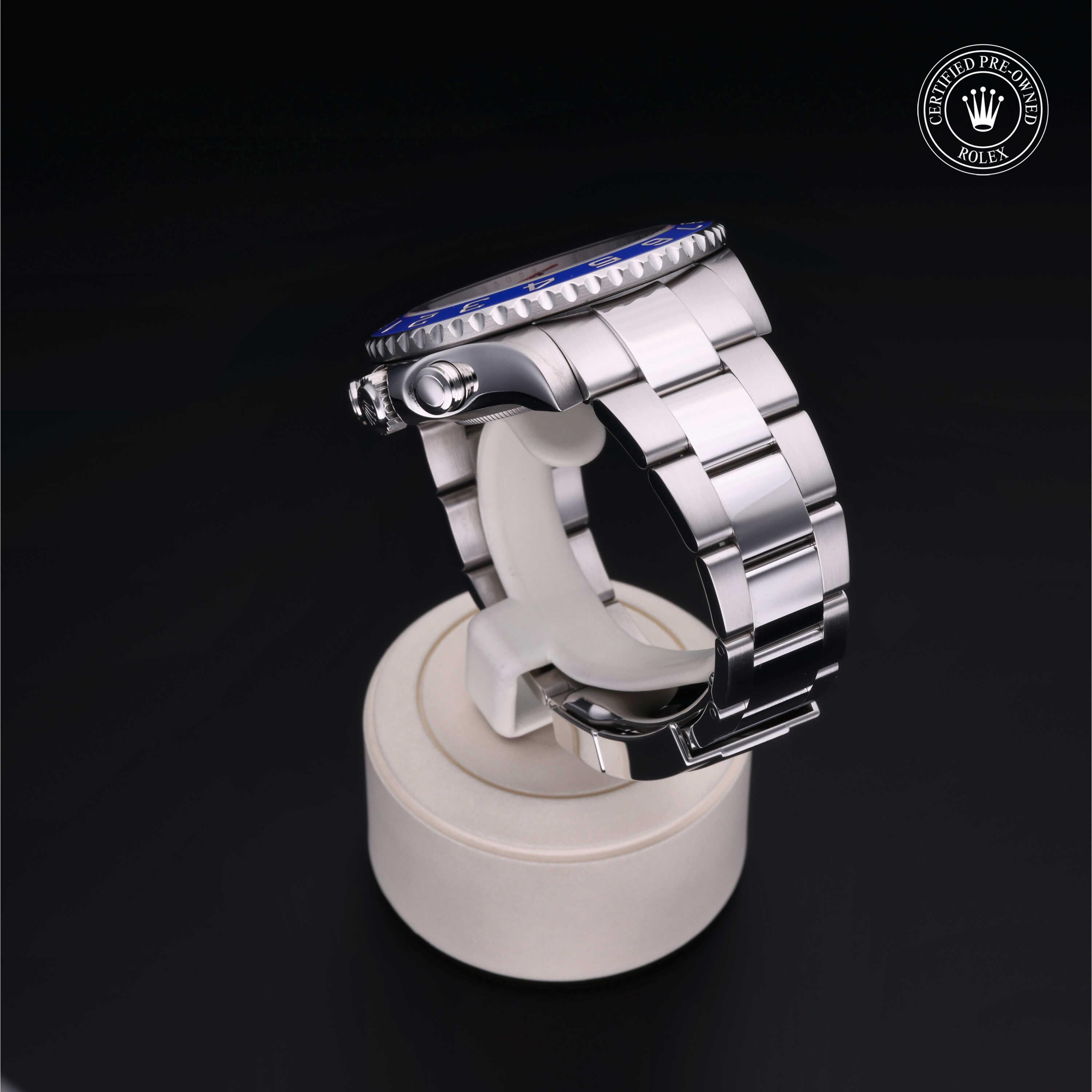 Side view of a stainless steel Rolex watch with a blue bezel displayed on a white stand against a black background, highlighting its luxury design and craftsmanship.