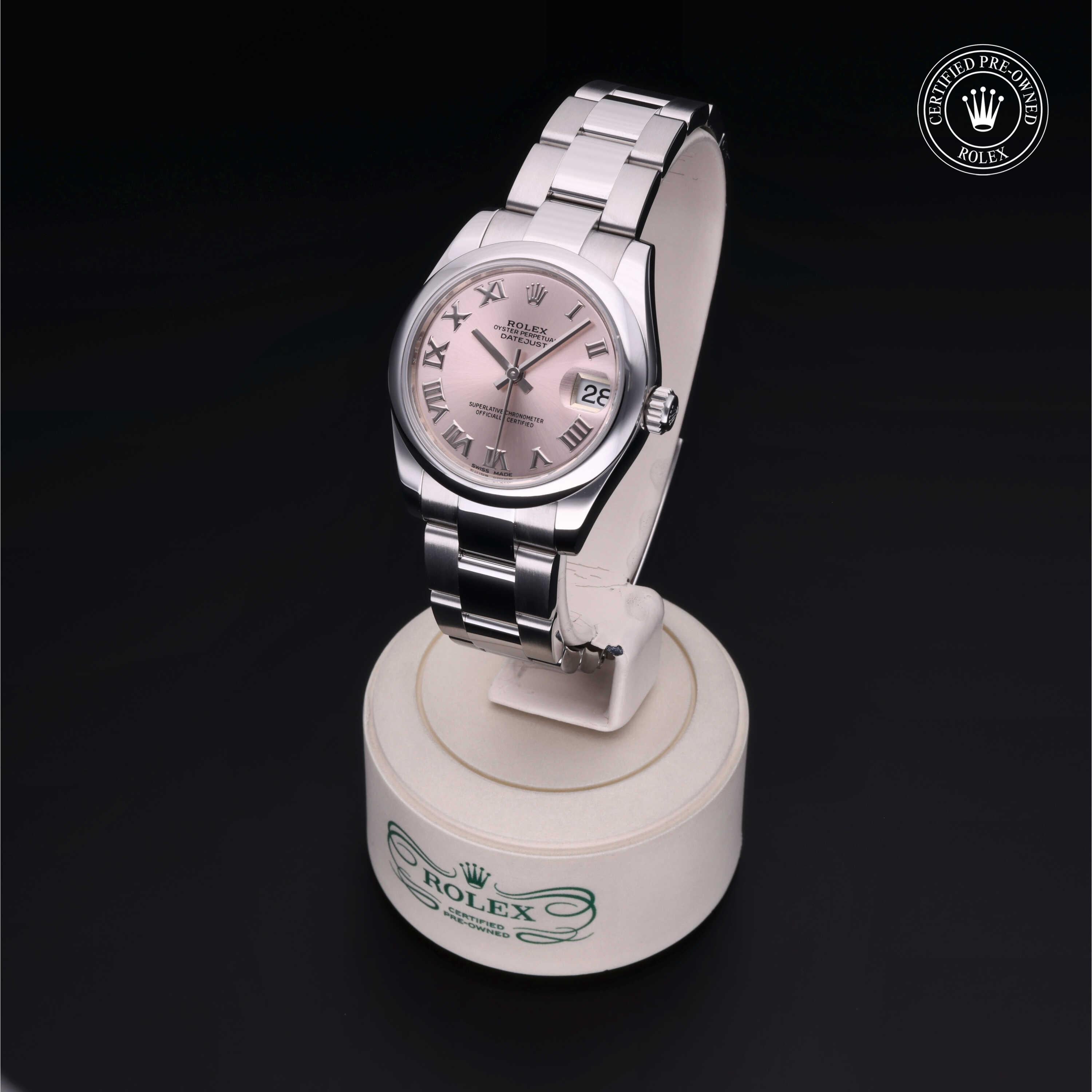 Rolex Certified Pre-Owned watch with a silver metal bracelet and pink dial featuring Roman numerals, displayed on a white stand against a black background.