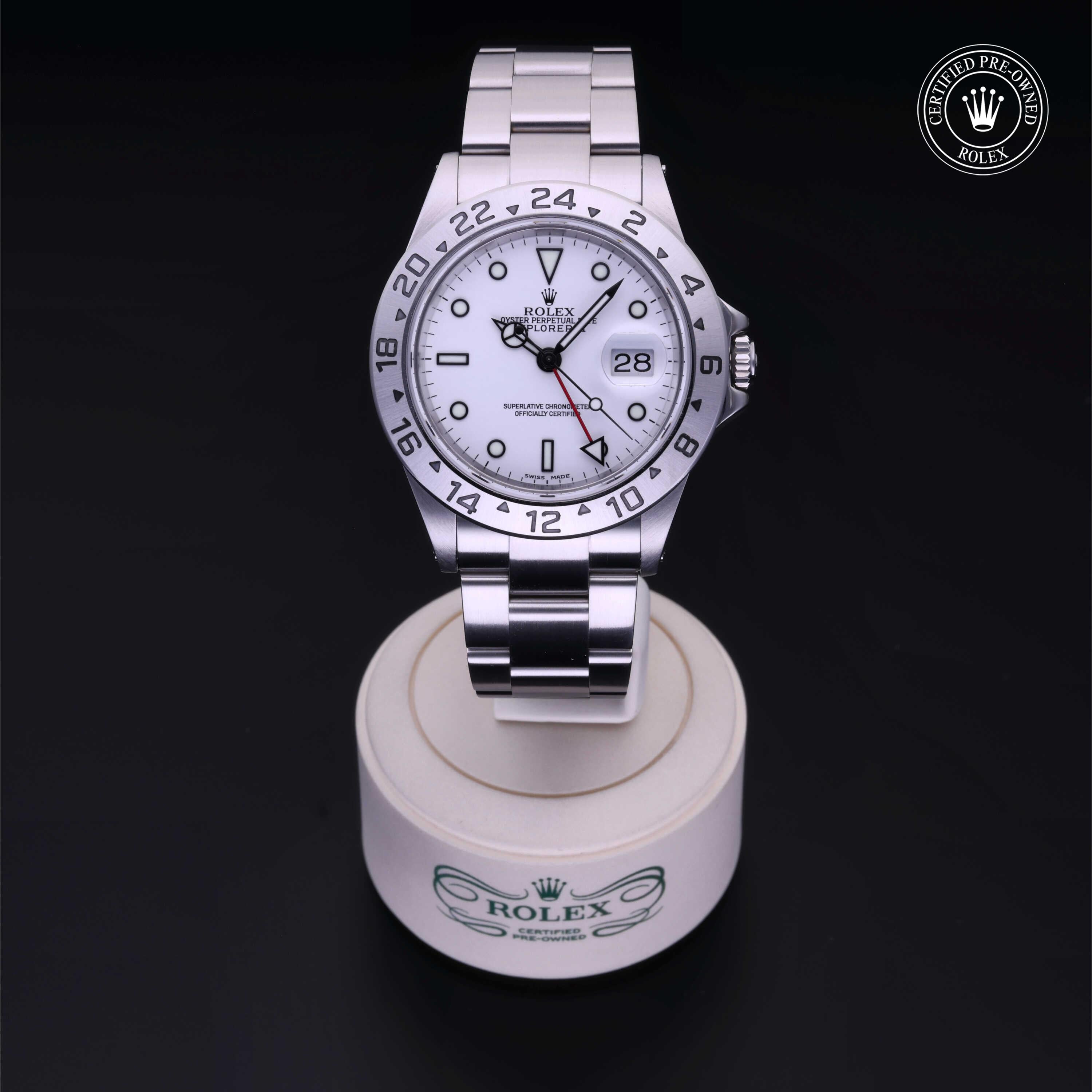 Silver Rolex luxury watch with white dial, black hour markers, and date display, shown on a branded stand with certified pre-owned Rolex logo in the corner, highlighting fine jewelry craftsmanship.