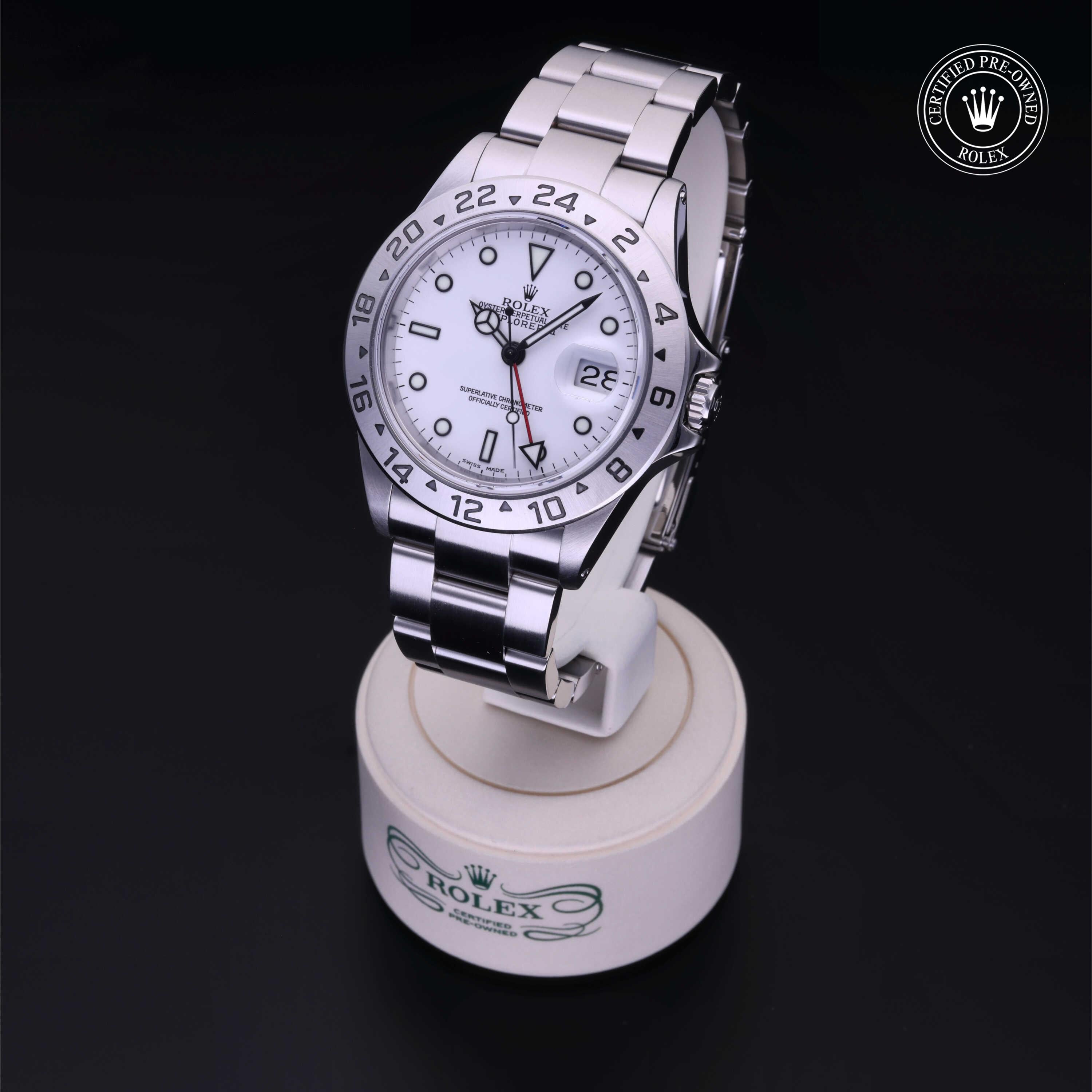 Stainless steel luxury watch with a white dial, black hour markers, red GMT hand, and date display on a branded Rolex stand, highlighting precision craftmanship.