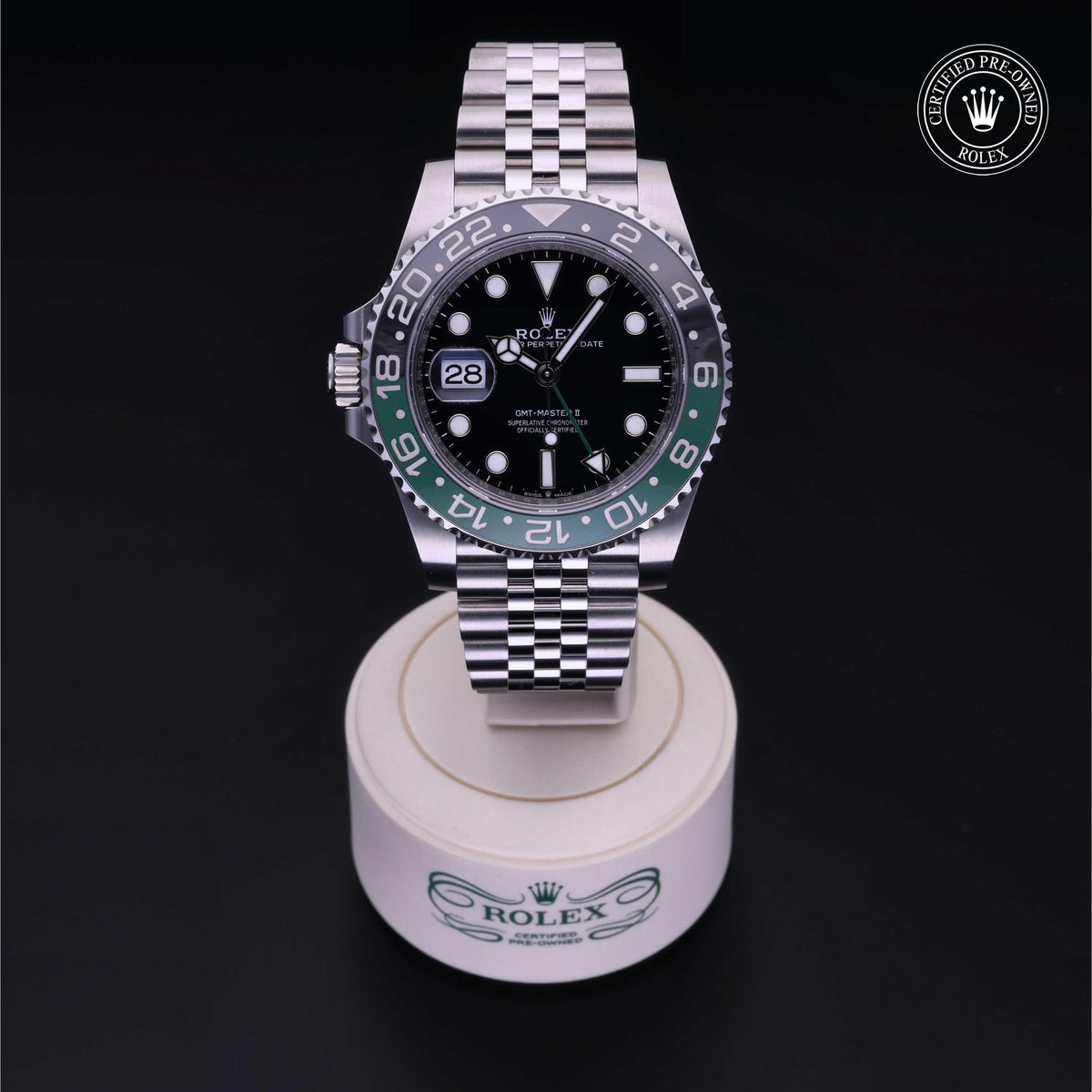 Rolex GMT-Master II luxury watch with black and green bezel, silver jubilee bracelet, displayed on a branded stand with certified pre-owned Rolex logo in the corner.