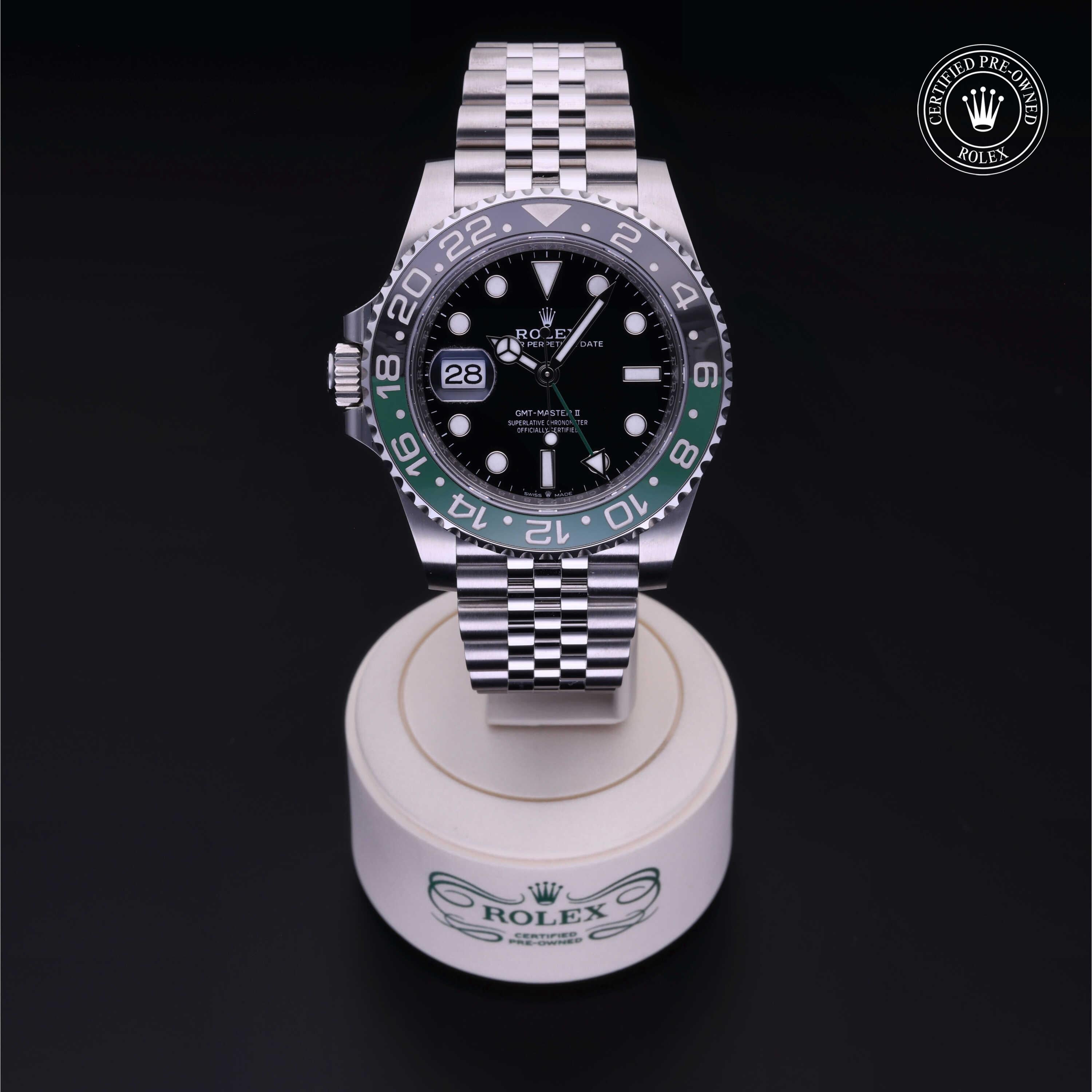 Rolex GMT-Master II luxury watch with black and green bezel, silver jubilee bracelet, displayed on a branded stand with certified pre-owned Rolex logo in the corner.