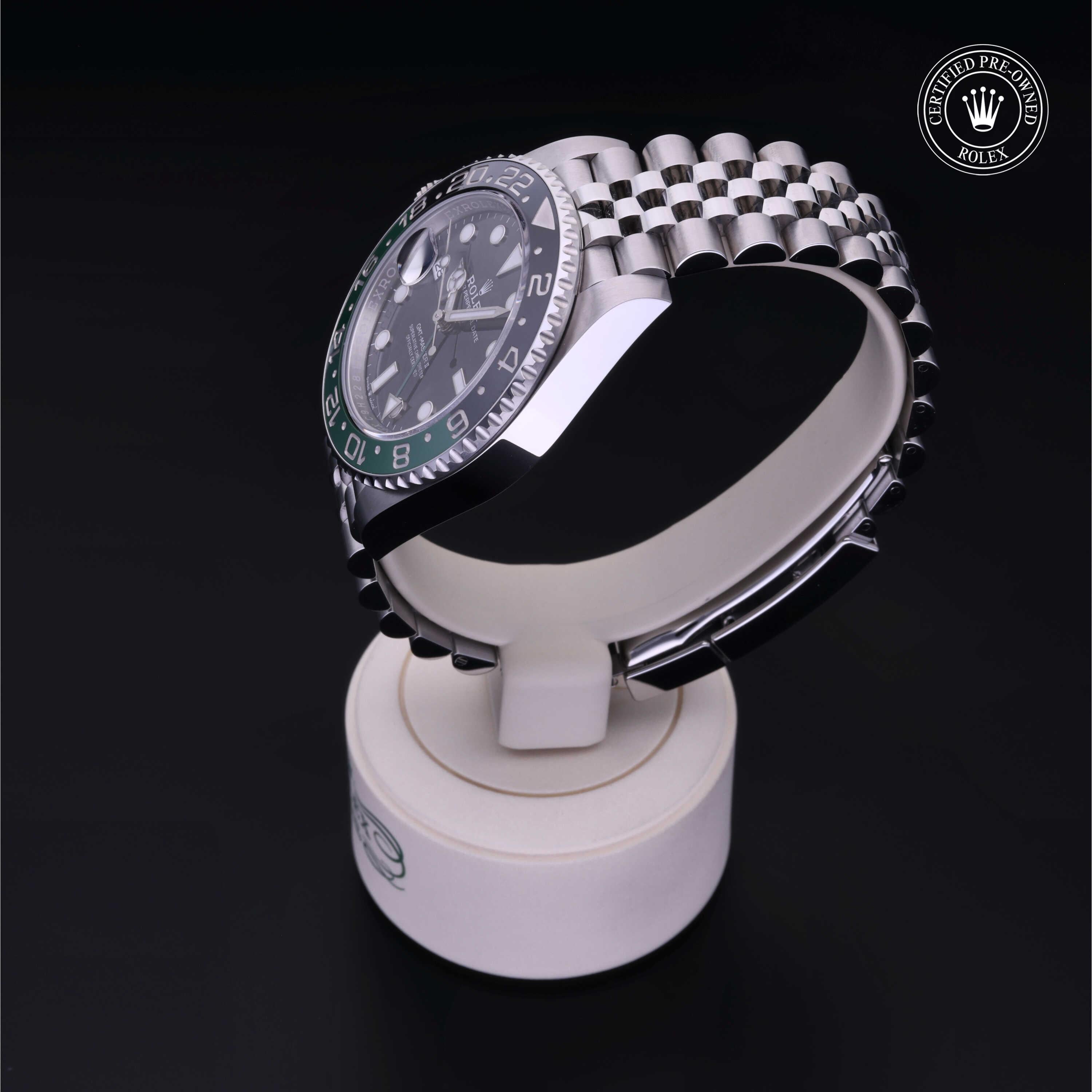 Stainless steel Rolex luxury watch with black and green bezel and jubilee bracelet displayed on a white stand against a dark background, certified pre-owned.