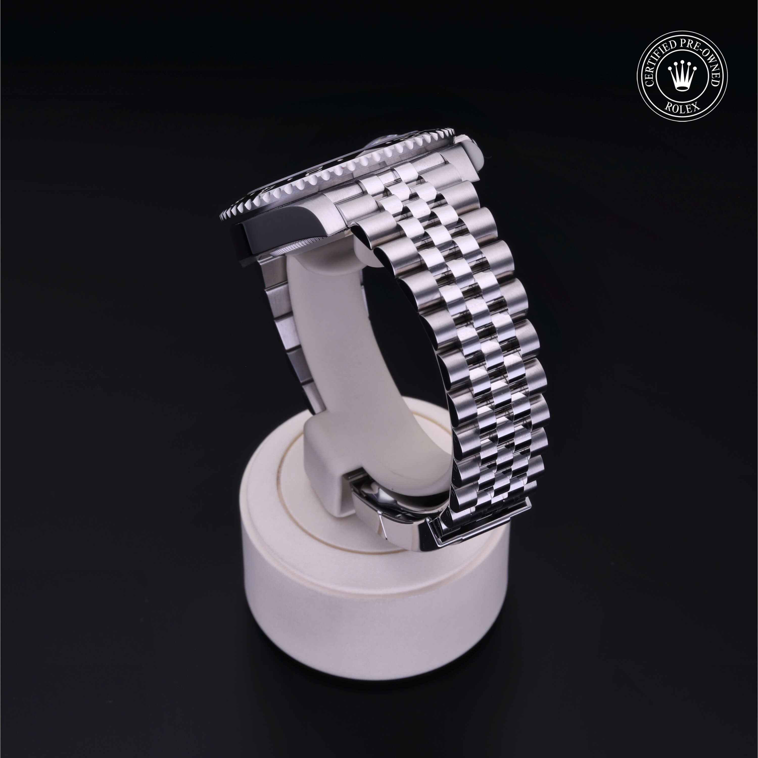 Close-up of a polished silver luxury watch band displayed on a white stand against a dark background, featuring a certified pre-owned Rolex emblem.