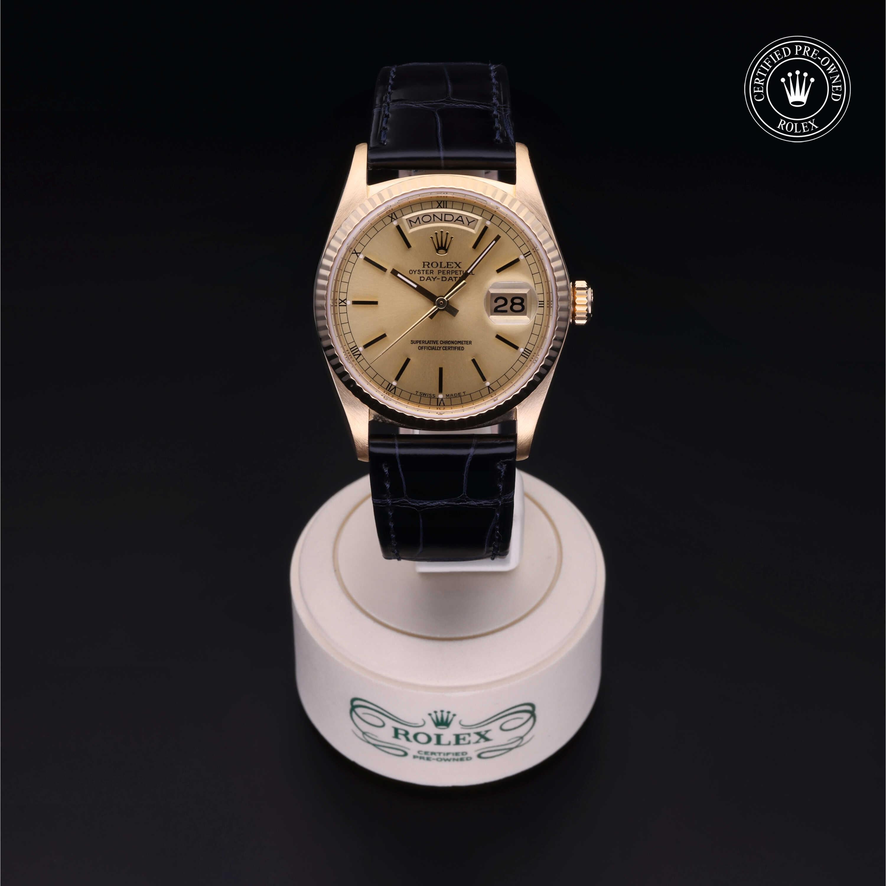 Luxurious gold Rolex watch with a beige dial, black leather strap, and day-date display, presented on a branded stand against a dark background.