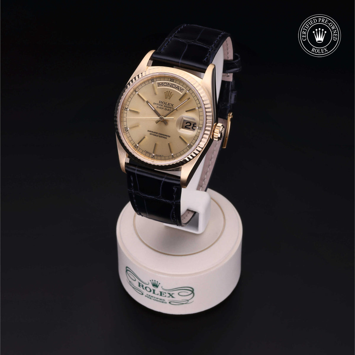 Luxury gold Rolex watch with a black leather strap displayed on a white stand, featuring a date window and a 