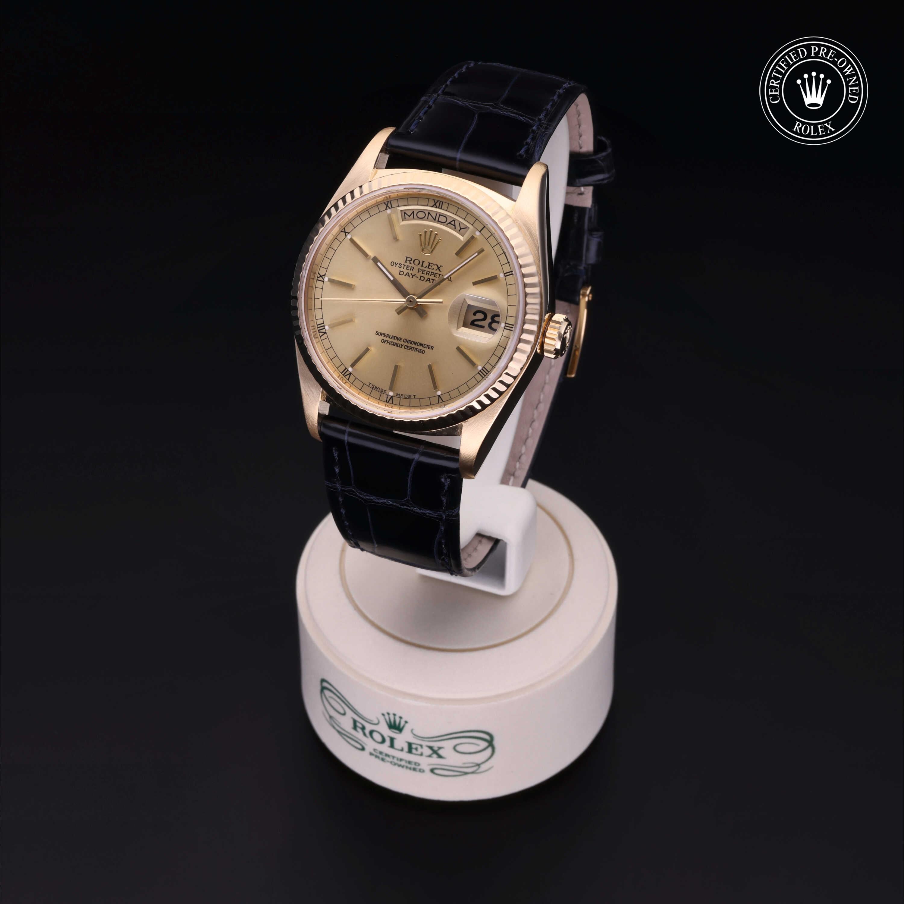 Luxury gold Rolex watch with a black leather strap displayed on a white stand, featuring a date window and a 