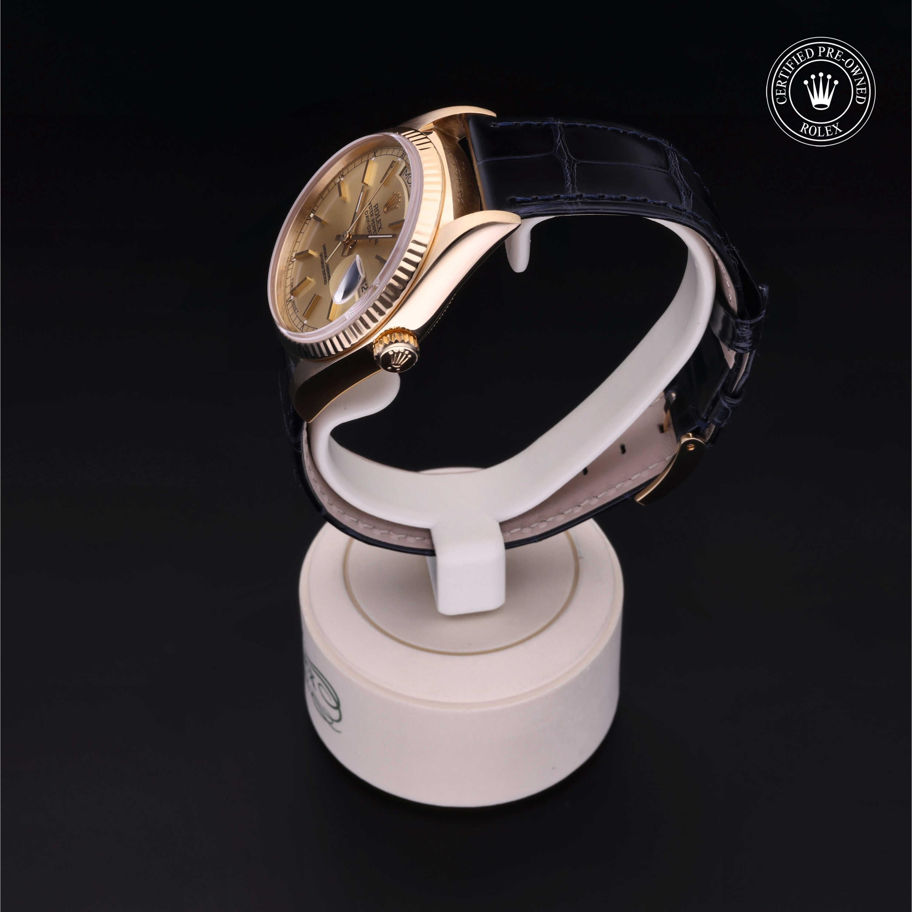 Close-up of a gold Rolex wristwatch with a tan dial and black leather strap displayed on a white stand, accompanied by a Certified Pre-Owned Rolex logo in the corner.