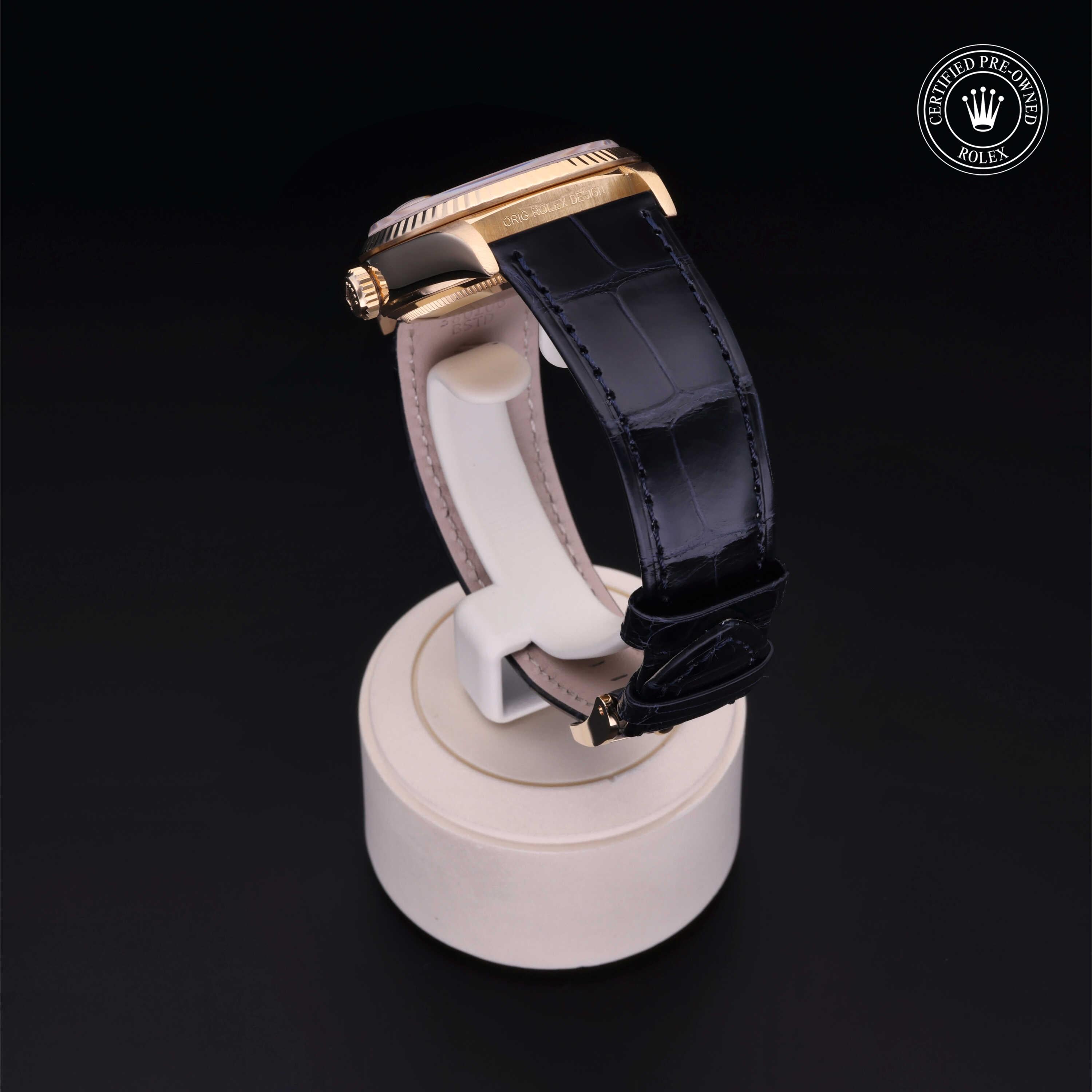 Side view of a luxury watch with a rose gold case and black alligator leather strap displayed on a white stand against a black background, featuring a certified pre-owned Rolex emblem.