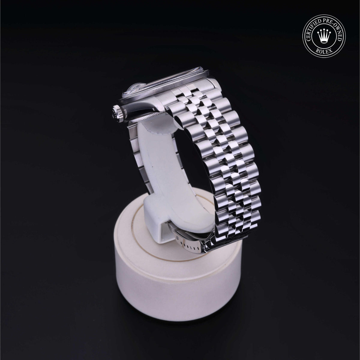 A polished silver metal watch bracelet with a Jubilee-style link design displayed on a cylindrical white stand against a black background, featuring a Rolex Certified Pre-Owned logo.