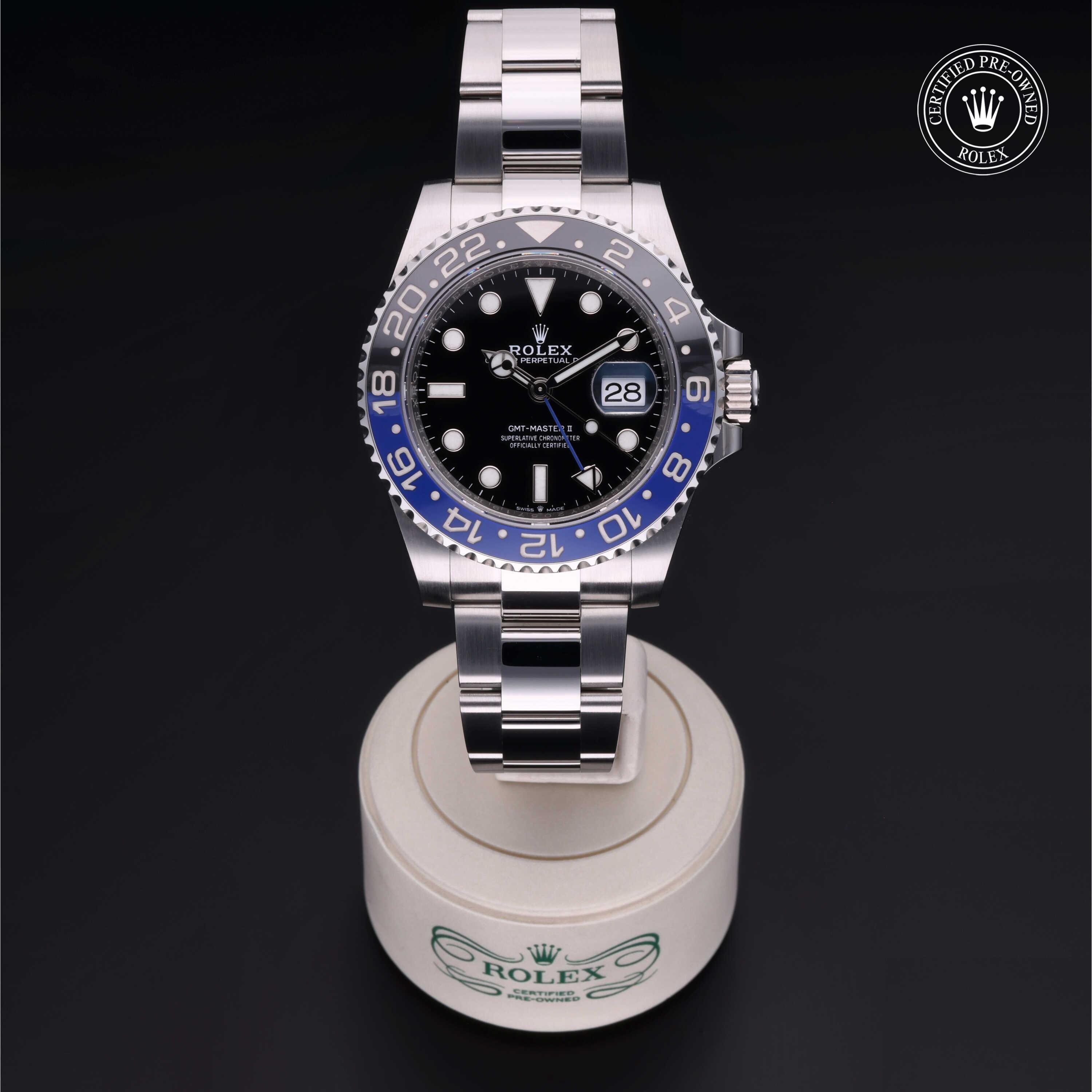 Rolex GMT-Master II watch with black and blue bezel, stainless steel bracelet, and date display on a white stand against a dark background, certified pre-owned.