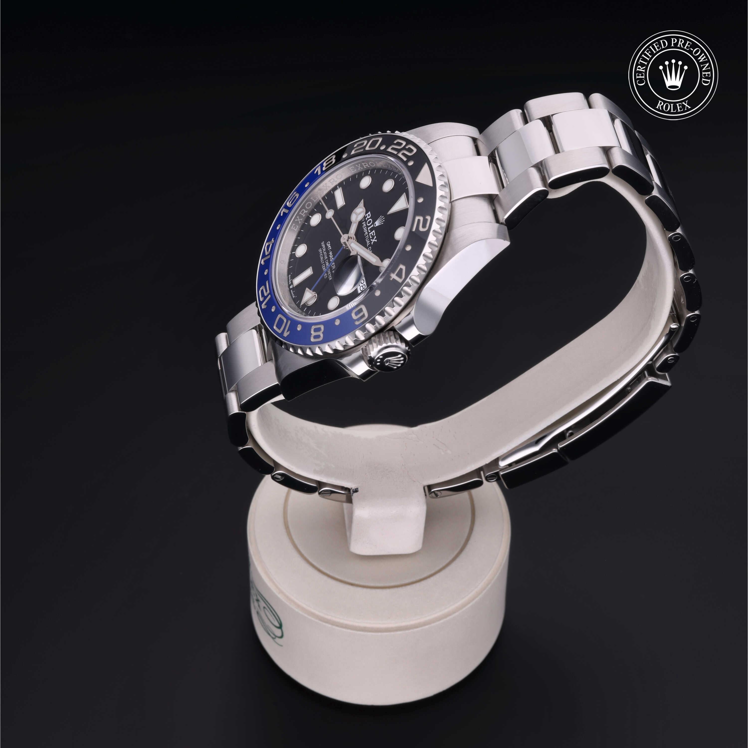Silver and black luxury watch with a blue and black bezel displayed on a white stand, featuring Rolex Certified Pre-Owned logo in the corner.