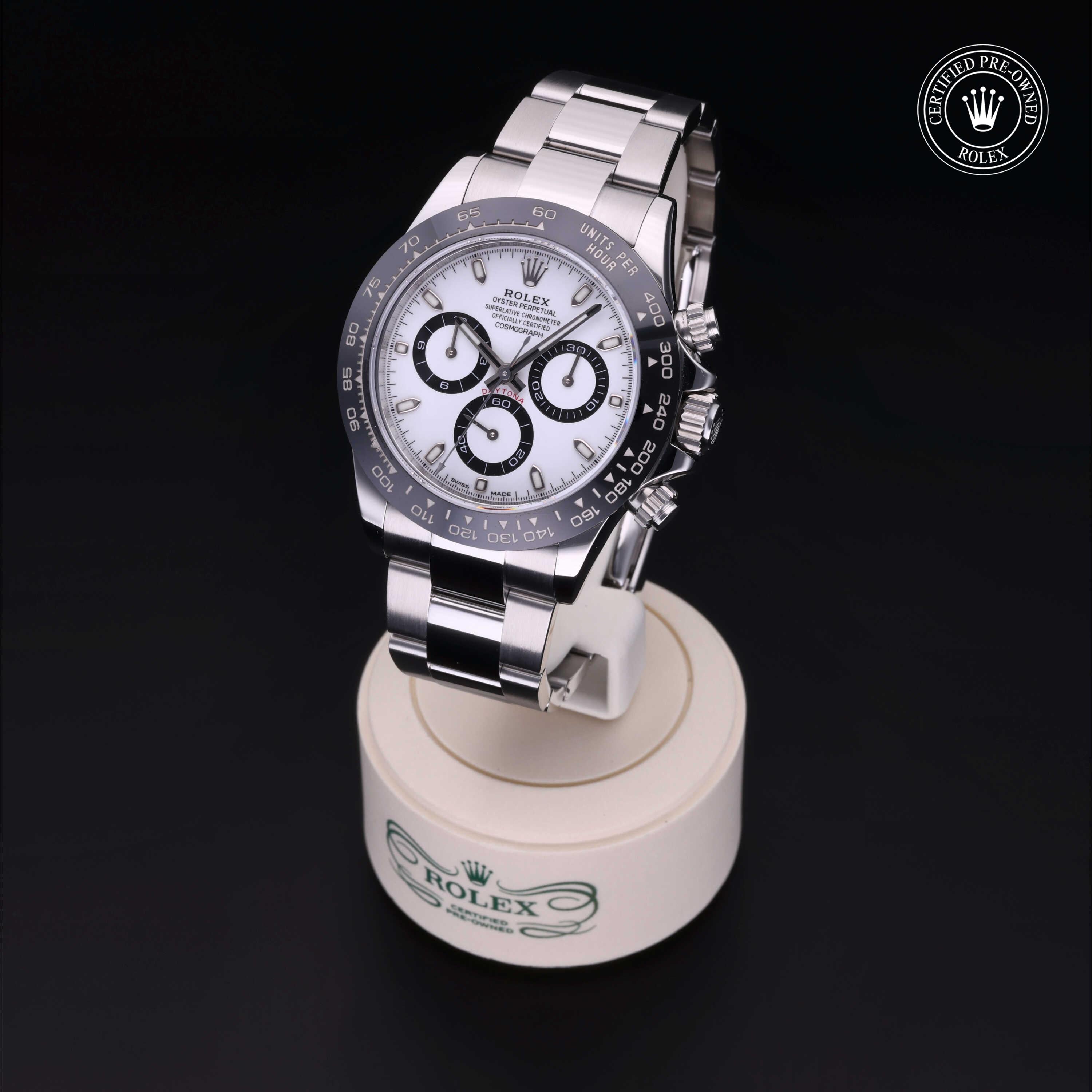 Rolex luxury stainless steel wristwatch with white dial and black subdials displayed on a branded stand against a black background, showcasing fine craftsmanship.