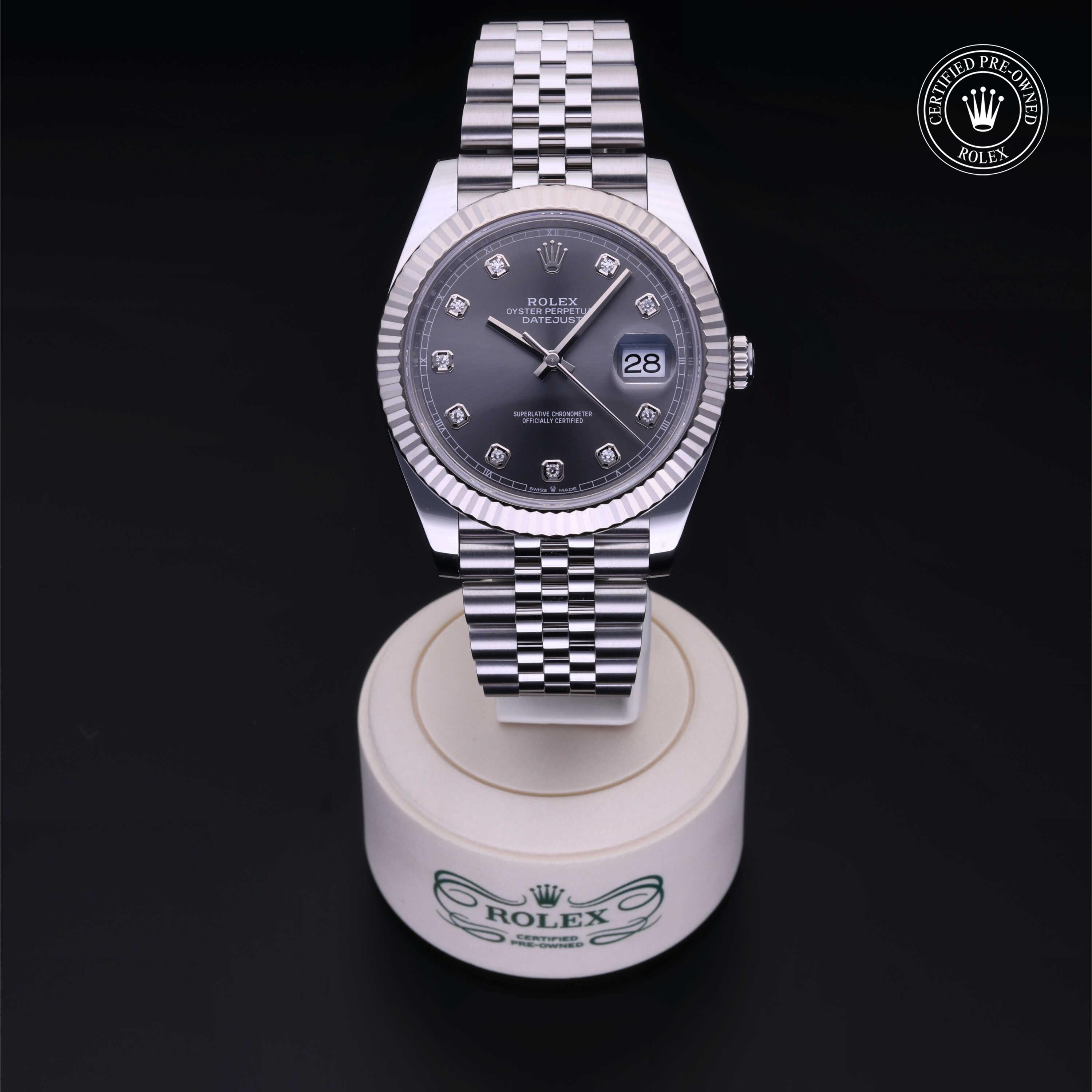 Rolex Datejust watch with silver jubilee bracelet, dark gray dial featuring diamond hour markers, displayed on a branded white stand with a certified pre-owned Rolex logo in the corner.