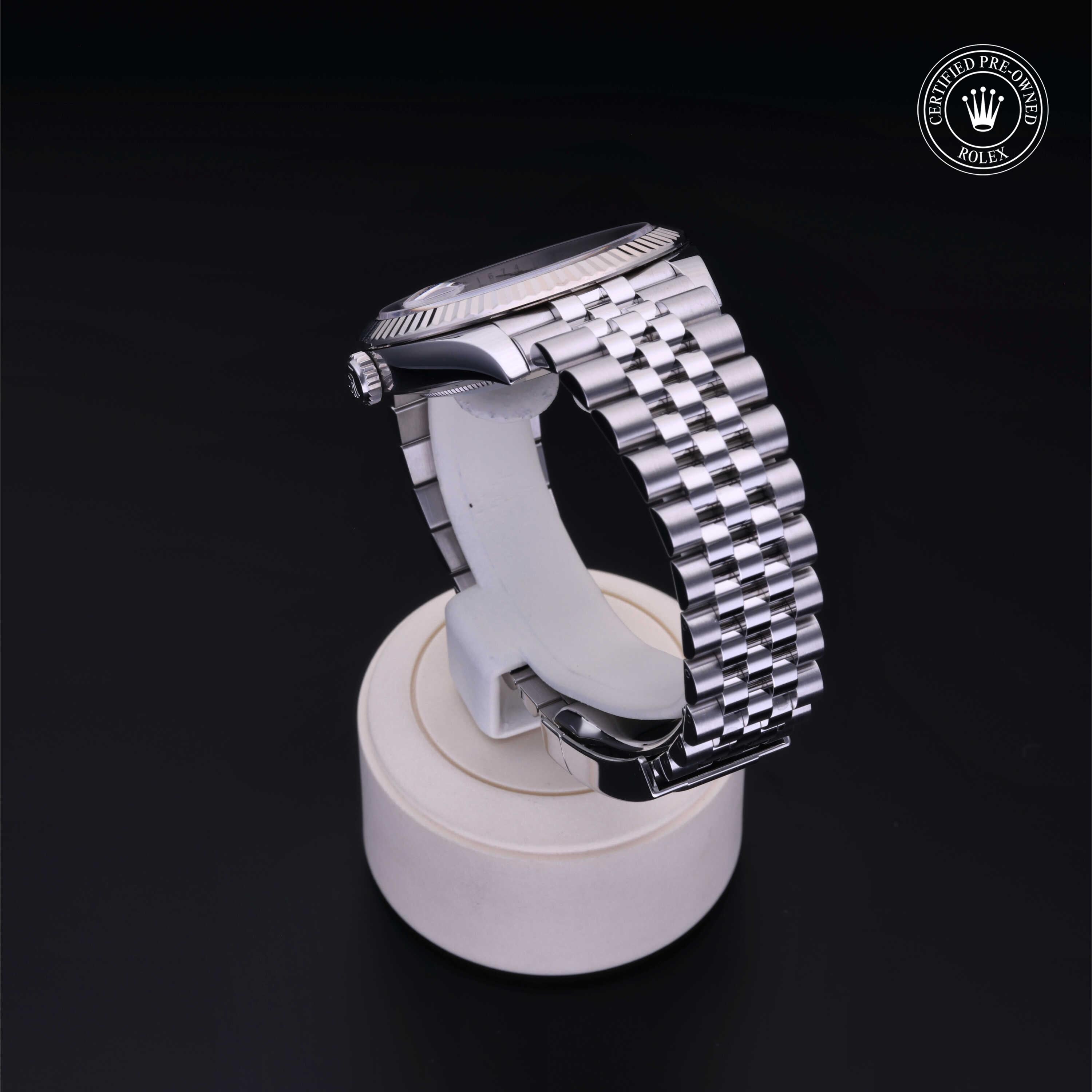Side view of a luxury Rolex watch with a polished silver metal bracelet displayed on a white stand against a black background, featuring a certified pre-owned emblem.