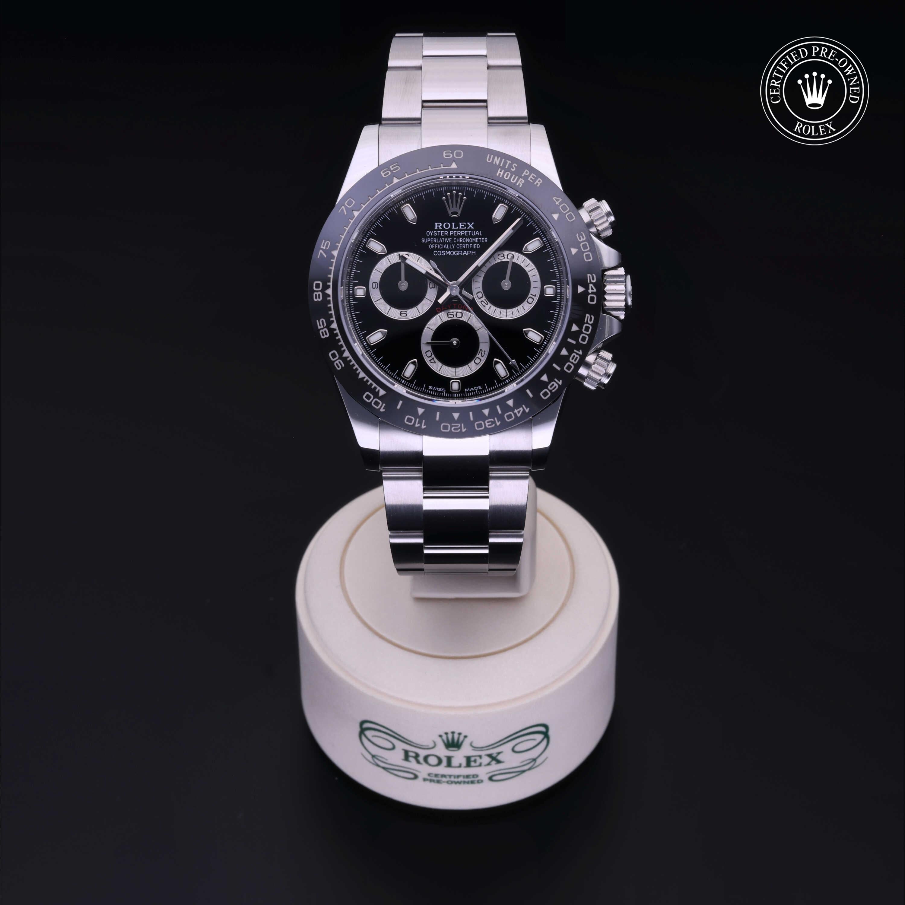 Rolex luxury watch with a stainless steel band and black dial featuring chronograph subdials, displayed on a branded stand with a certified pre-owned Rolex seal.