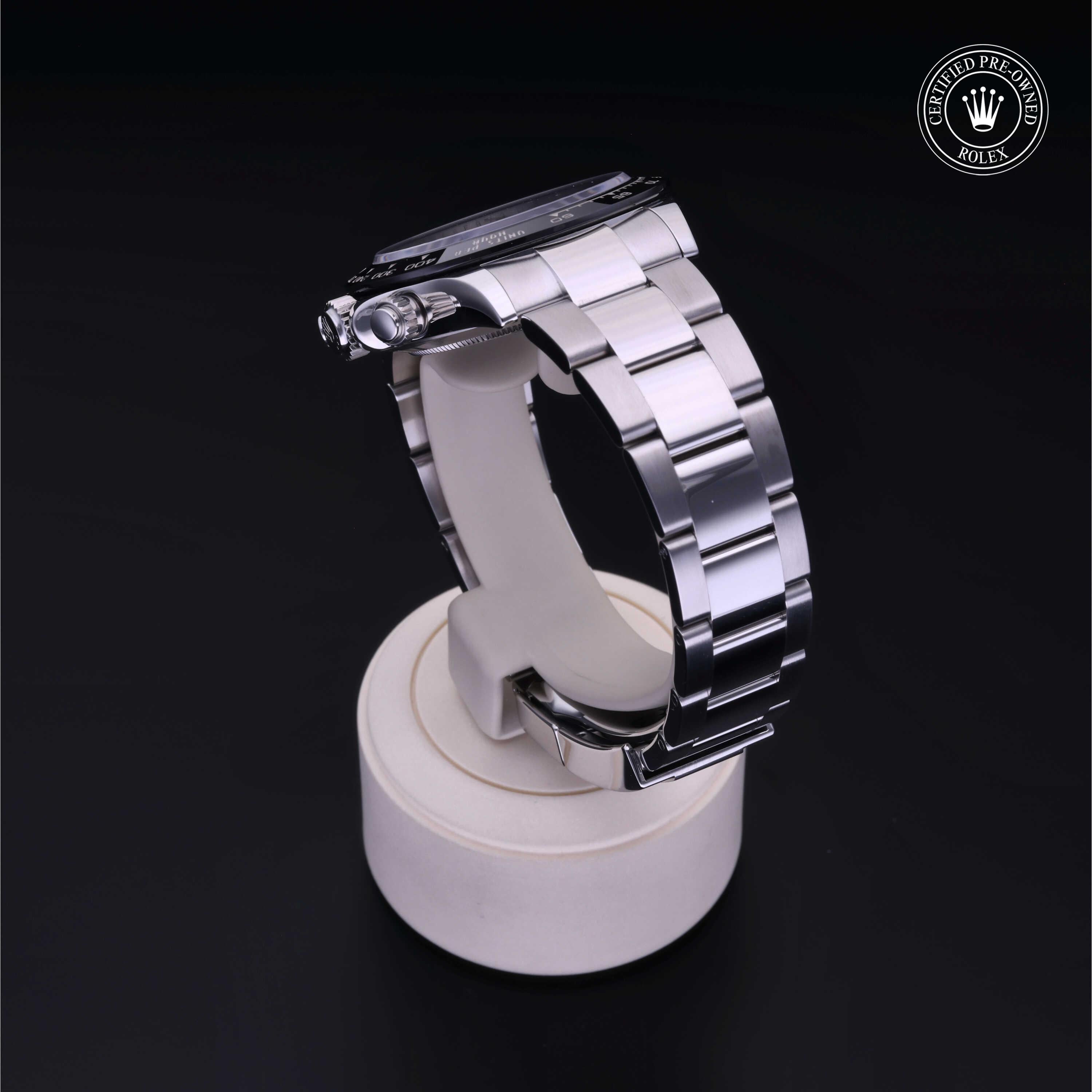 Side view of a polished stainless steel Rolex luxury watch displayed on a white stand against a dark background with a certified pre-owned Rolex logo in the corner.
