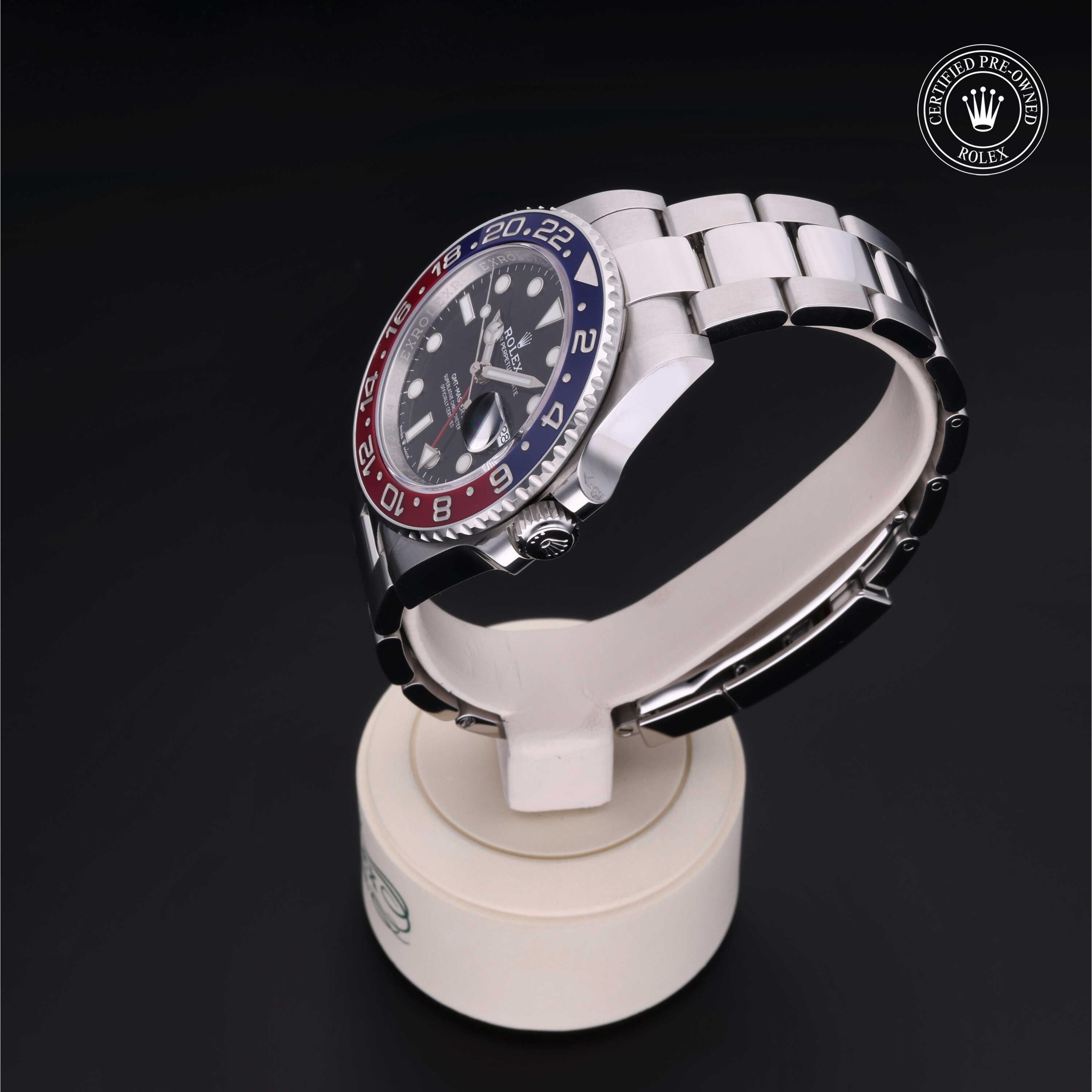 Stainless steel luxury watch with a red and blue bezel, black dial, and silver bracelet displayed on a white stand with a Certified Pre-Owned Rolex logo in the corner.