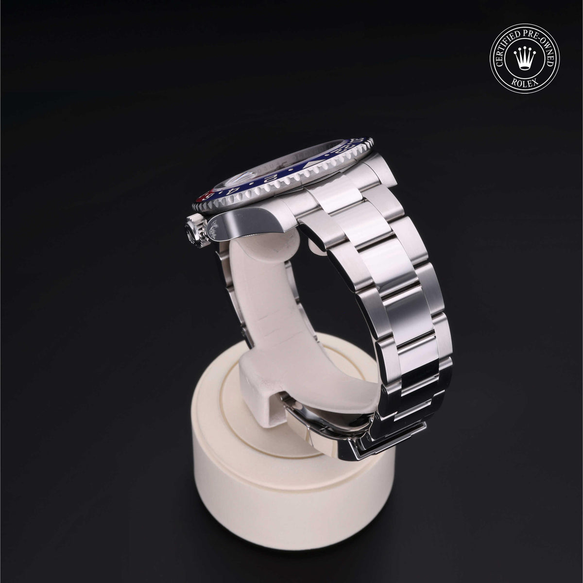 Silver stainless steel luxury watch with a blue and red bezel displayed on a white stand against a black background, featuring a Rolex Certified Pre-Owned logo.