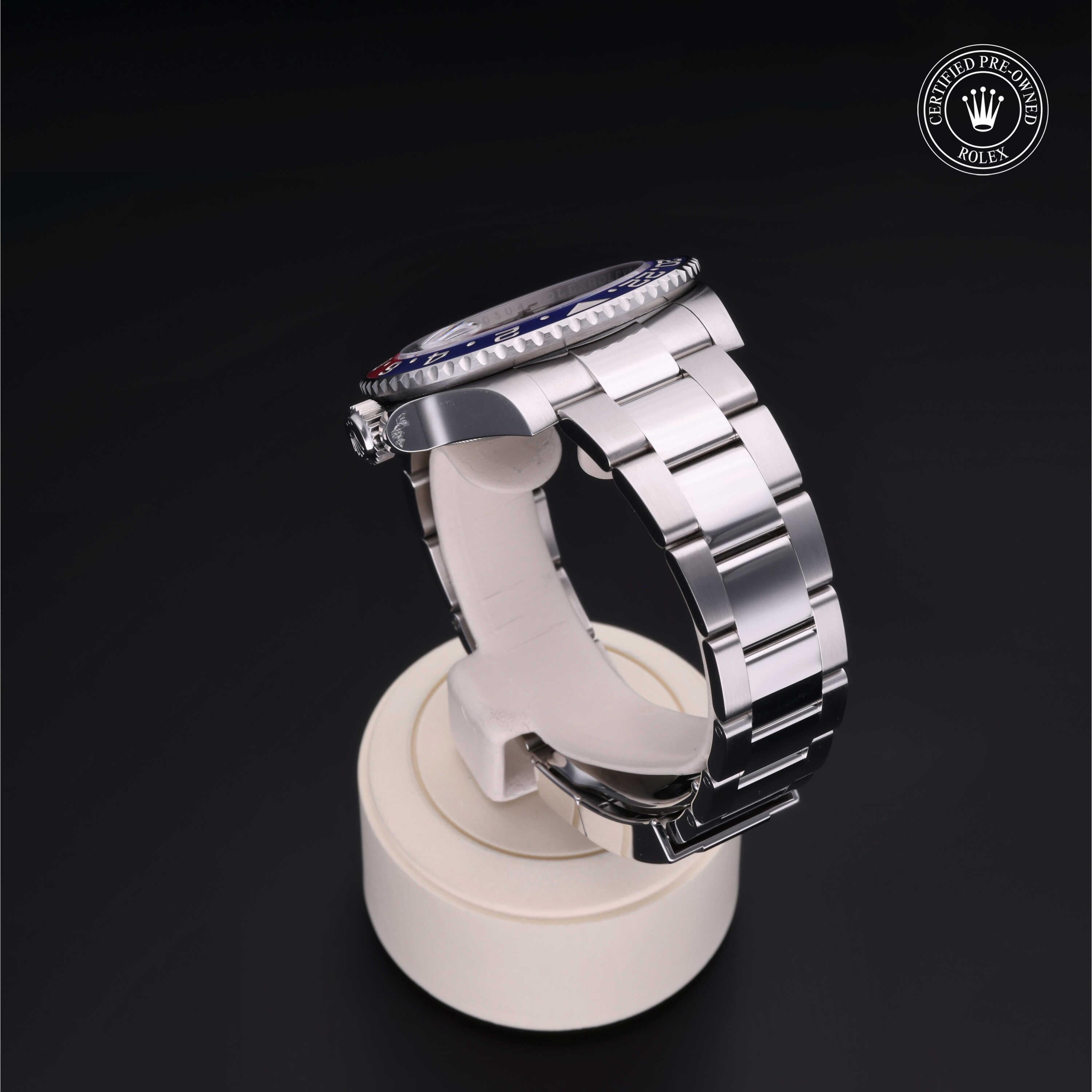 Silver stainless steel luxury watch with a blue and red bezel displayed on a white stand against a black background, featuring a Rolex Certified Pre-Owned logo.