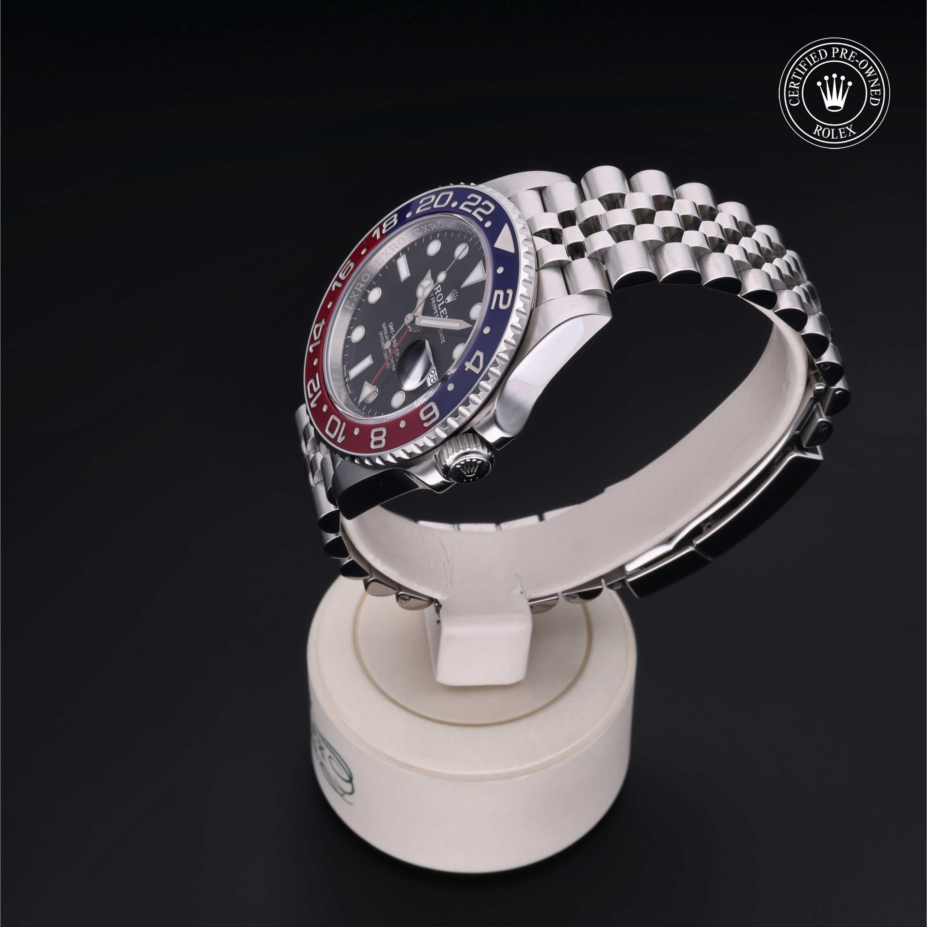 Close-up of a Rolex luxury watch with a red and blue bezel on a silver metal bracelet, displayed on a white stand with a Certified Pre-Owned Rolex logo above.