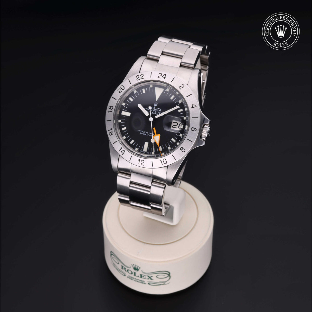 Rolex luxury watch with stainless steel bracelet and black dial on a white display stand, featuring a 24-hour bezel and a date window, certified pre-owned authentic timepiece.